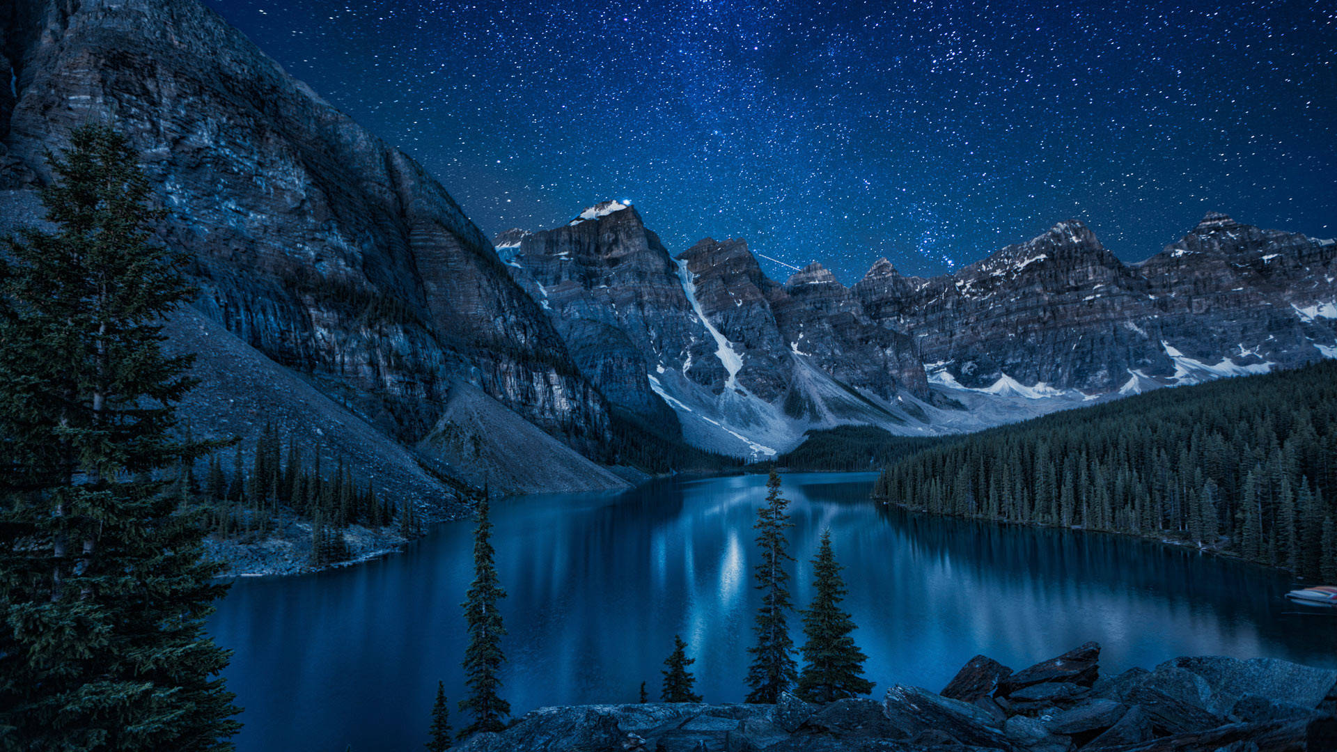 星空下的山間湖泊，周圍有積雪的山峰和常青樹。