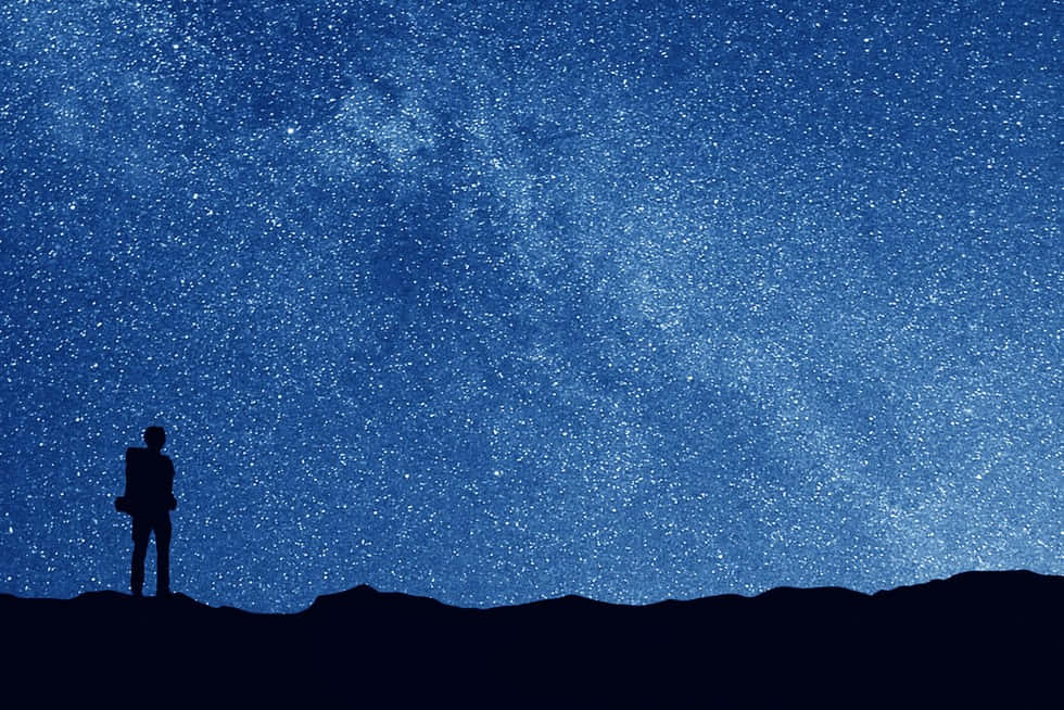 星空下的凝望天文攝影 壁紙 — 一個孤獨的身影站在黑暗的山丘上，仰望滿佈銀河的廣闊星空夜空。