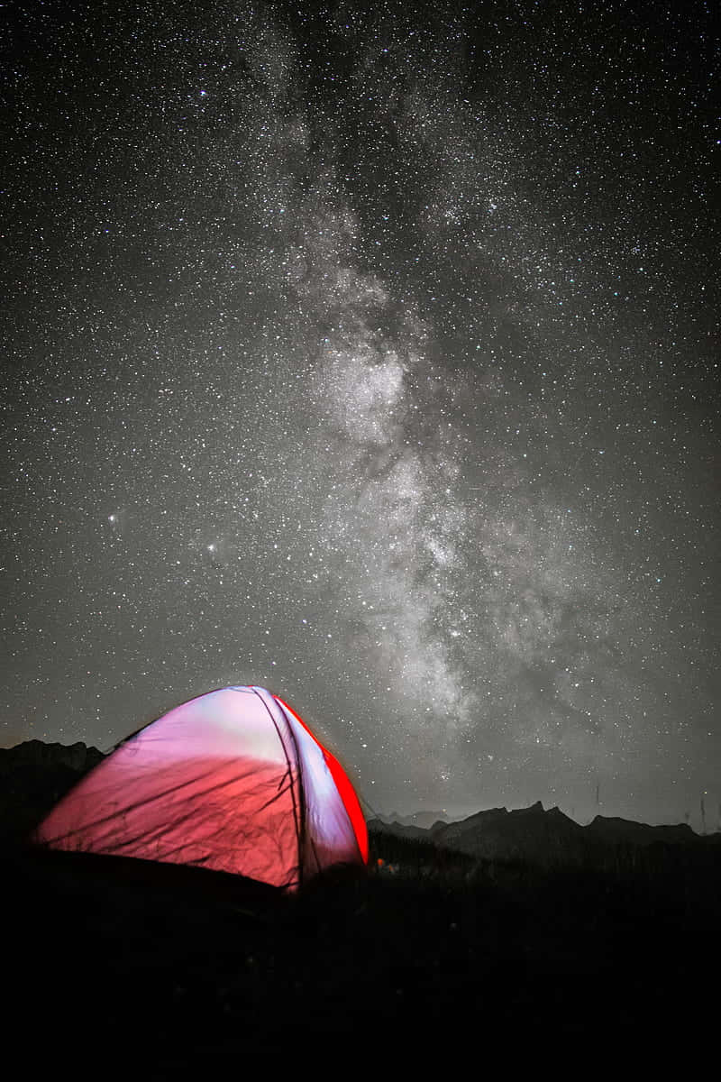 在星空下，一個紅色帳篷被照亮，銀河可見。