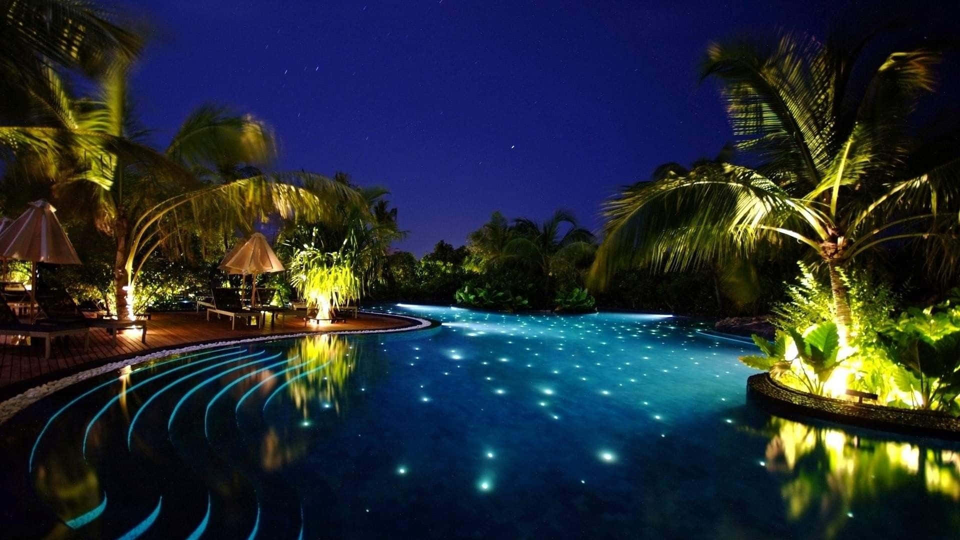 海灘 桌布 壁紙 — 星空下的無邊際泳池，在棕櫚樹和溫暖燈籠環繞的黑暗天空下，內置燈光閃爍。