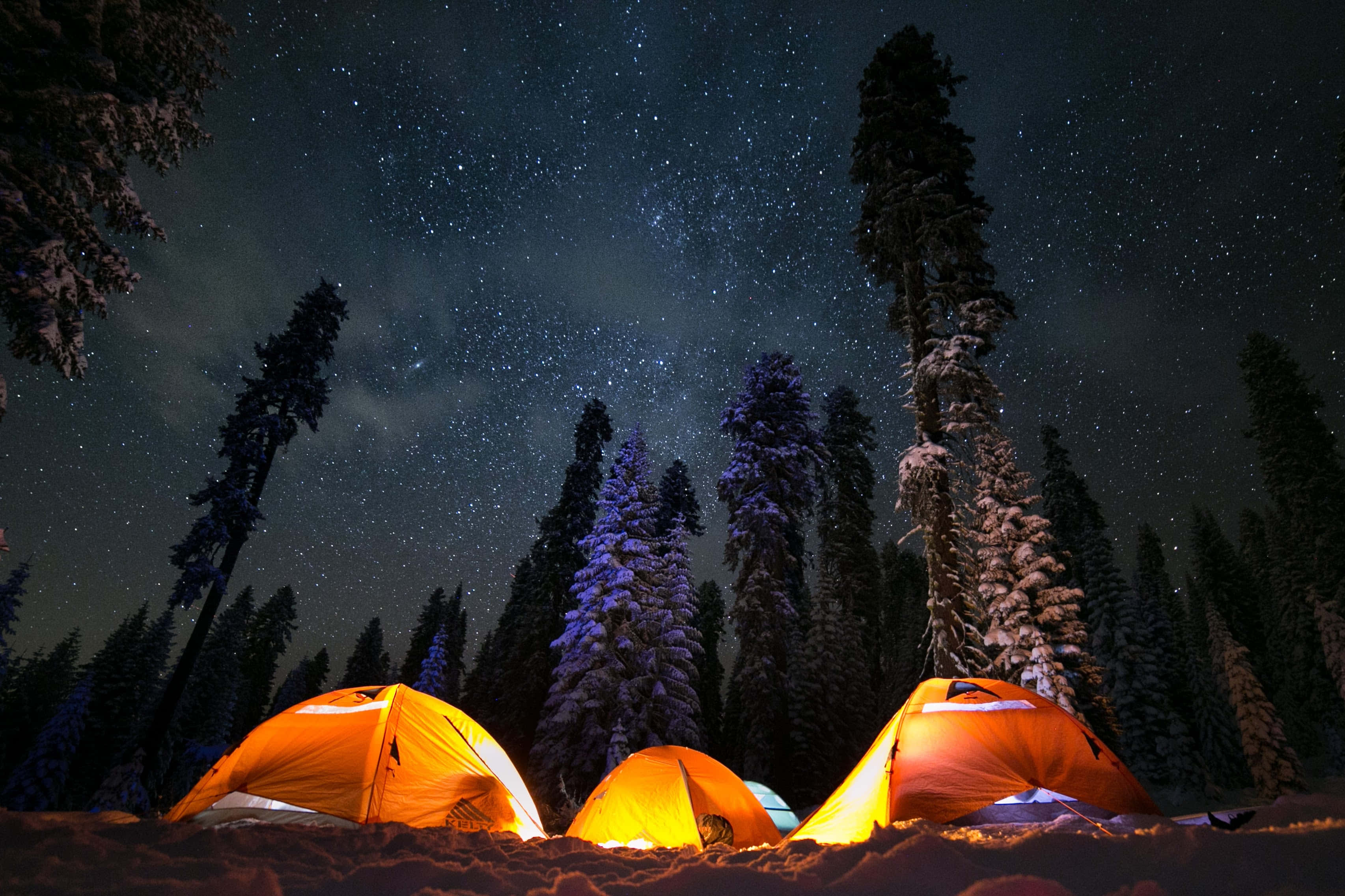 星空下的露營體驗 壁紙 — 三個發光的橙色帳篷，坐落在白雪覆蓋的森林中，星空下。