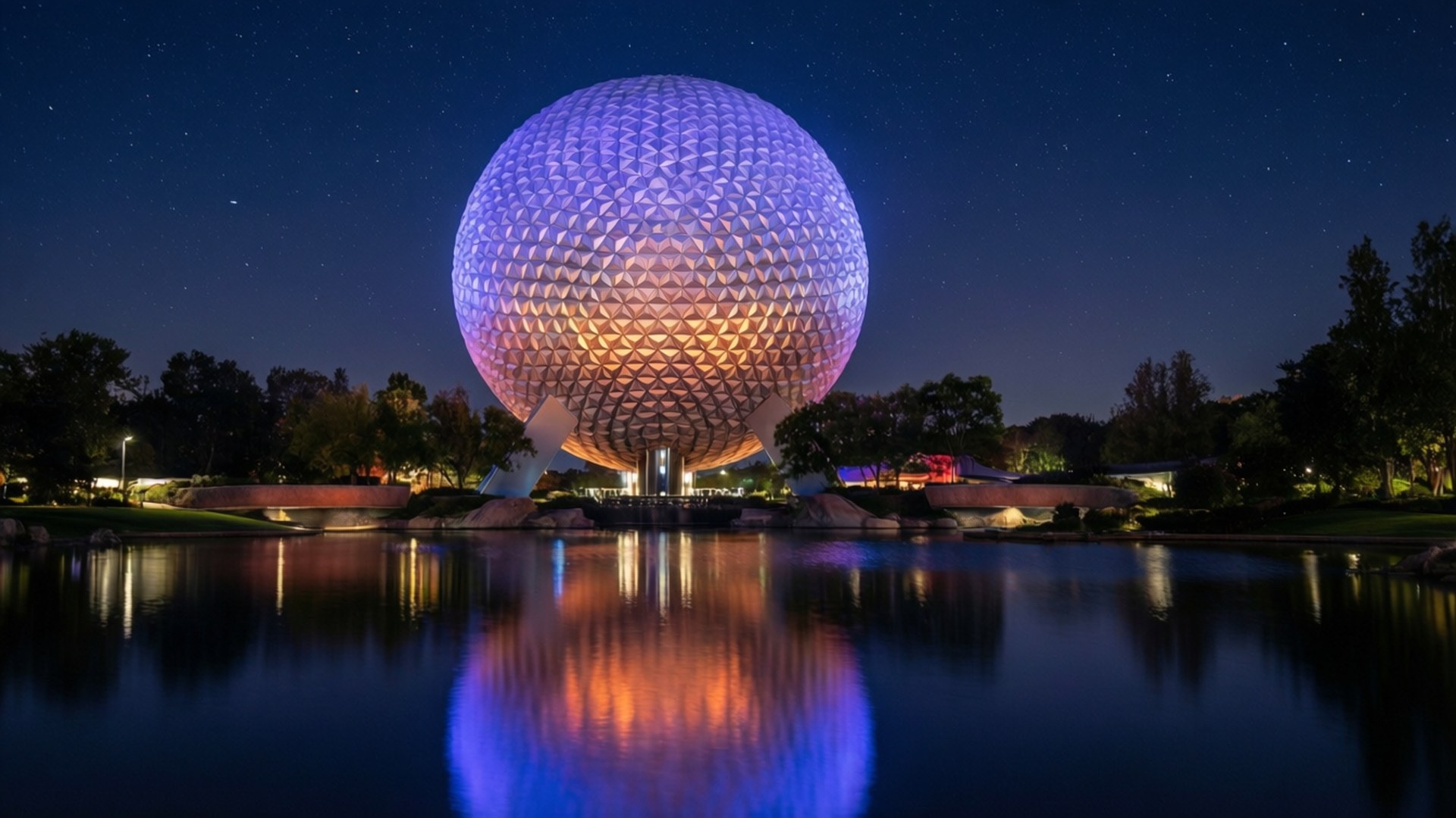 星空倒影下的Epcot球體 壁紙 — 一個巨大的發光測地線球體在繁星點點的夜空下閃耀著紫色和橙色，完美倒映在下方平靜的湖面上。