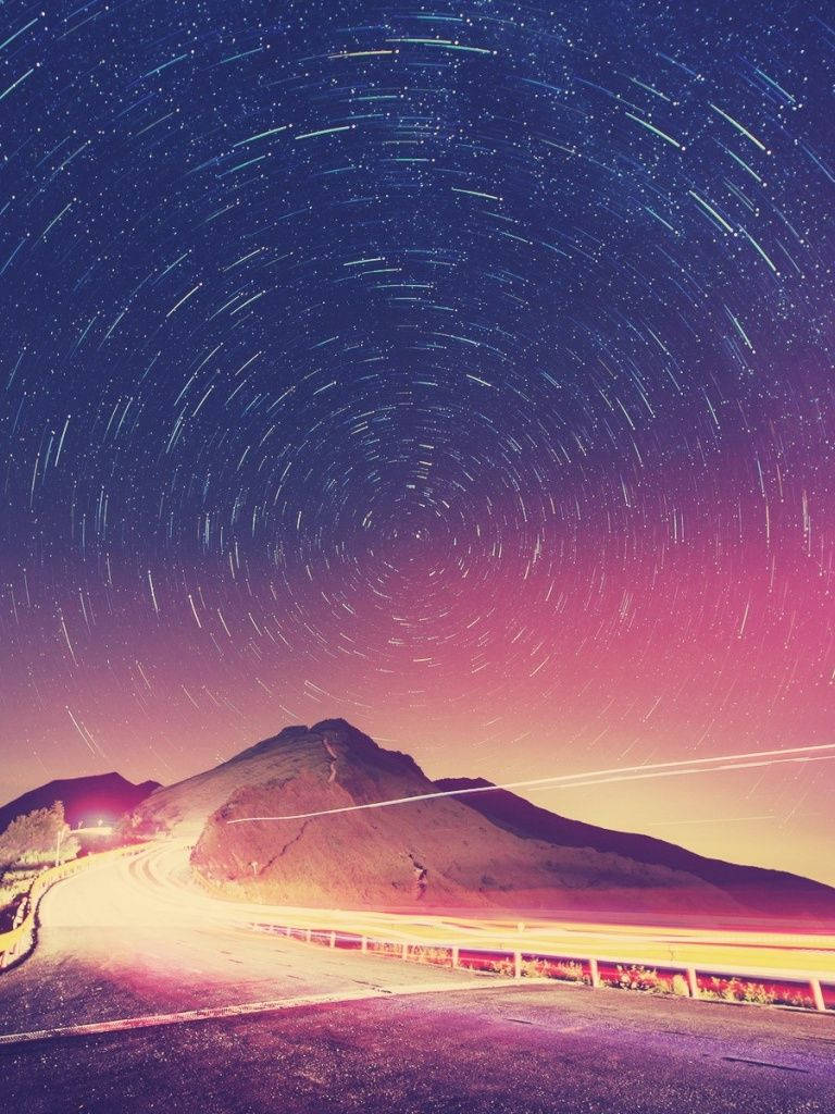 在帶有星軌和粉紫色調的天空下蜿蜒的山路。