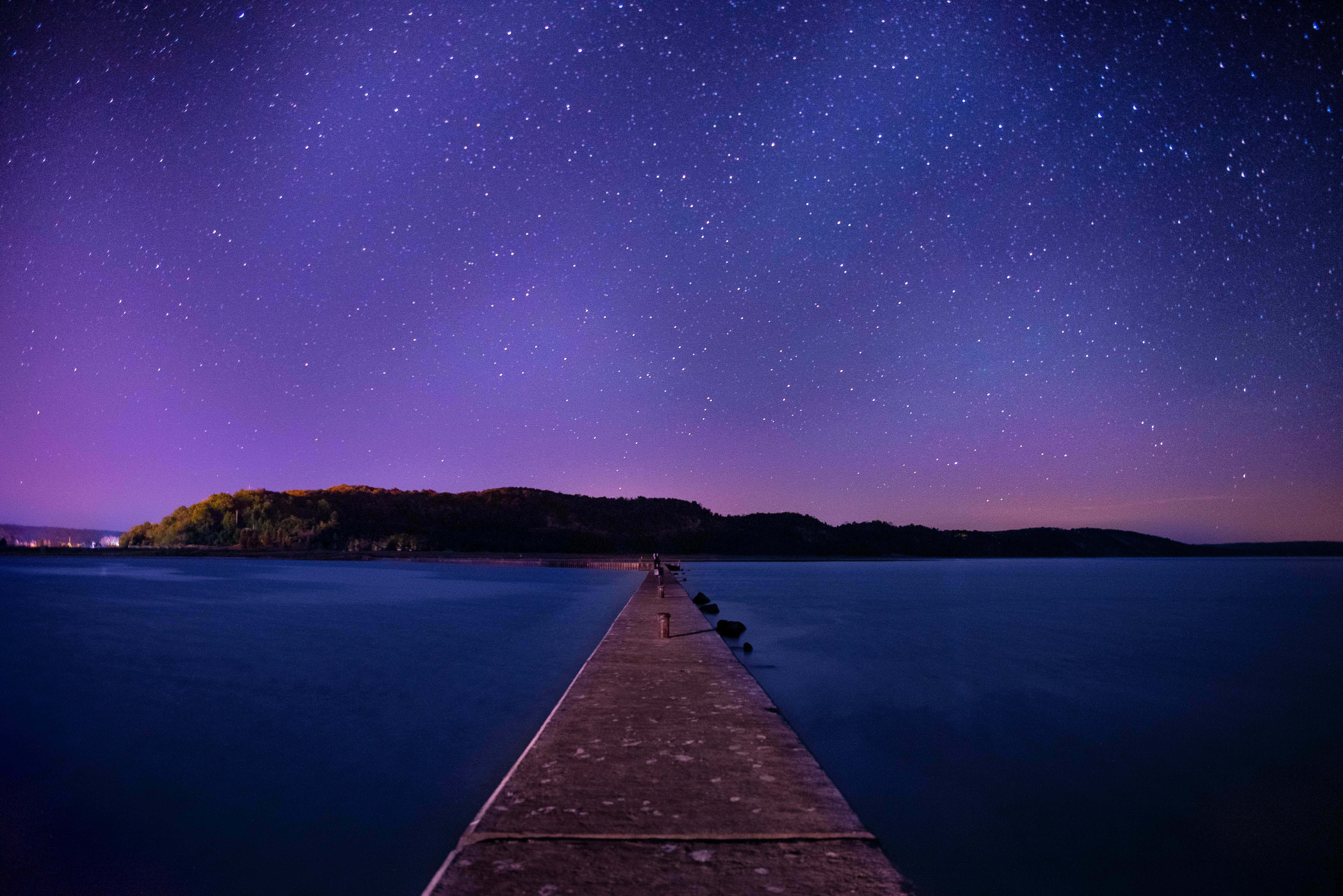 Horizon 桌布 壁紙 — 星空夜空在平靜的湖面上拱起，一條長長的混凝土碼頭伸向遠處的森林覆蓋的湖岸。