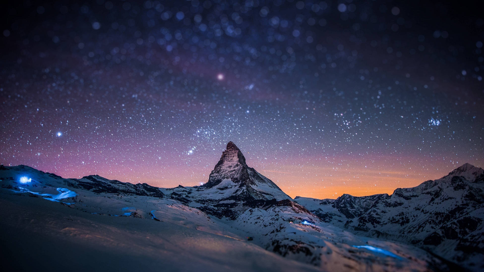 白雪覆蓋的山峰在紫色和橙色色調的星空暮色天空下。