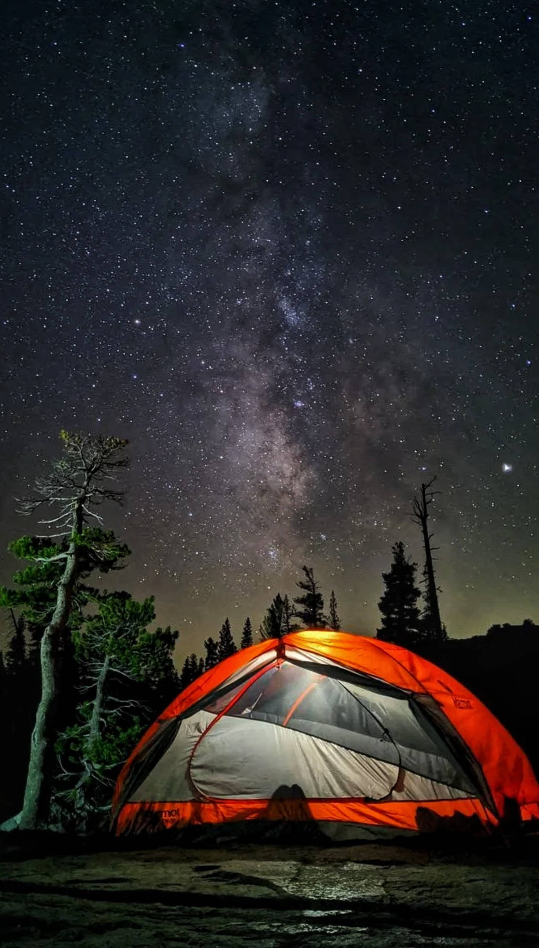 在繁星點點的夜空下，一個明亮的橙色帳篷，上方可見銀河。