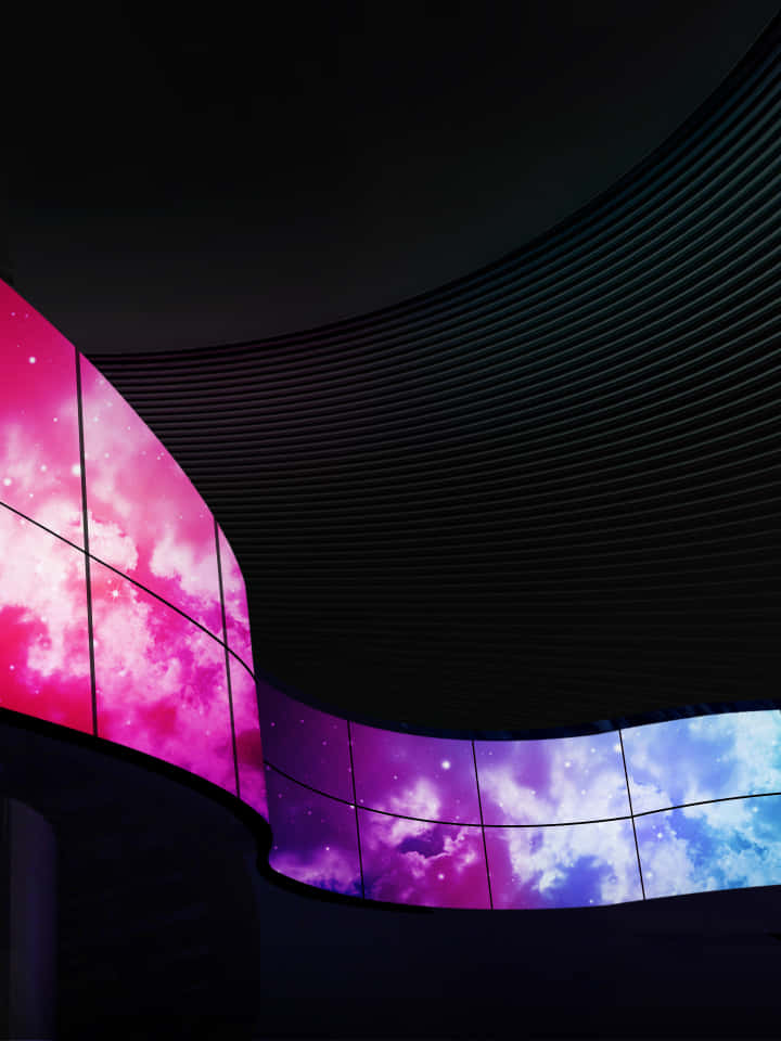 星系 OLED 圖 壁紙 — 彎曲的數碼屏幕在深色條紋天花板的襯托下，展示出充滿活力的粉紅色、紫色和藍色宇宙星雲。