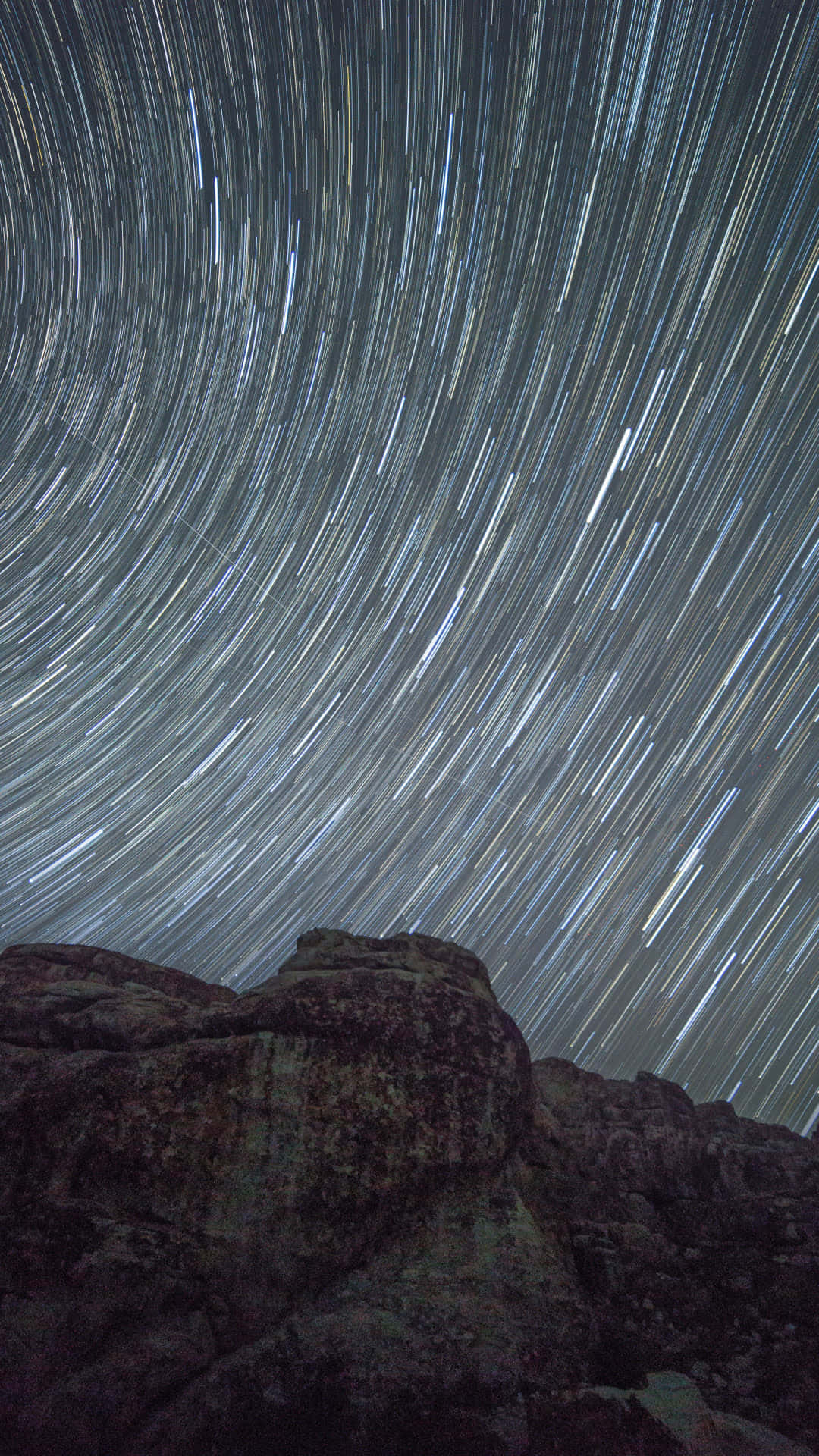 time lapse 桌布 壁紙 — 星軌在黑暗的天空中戲劇性地盤旋，越過崎嶇的山岩，這是一張長時間曝光的夜景照片。