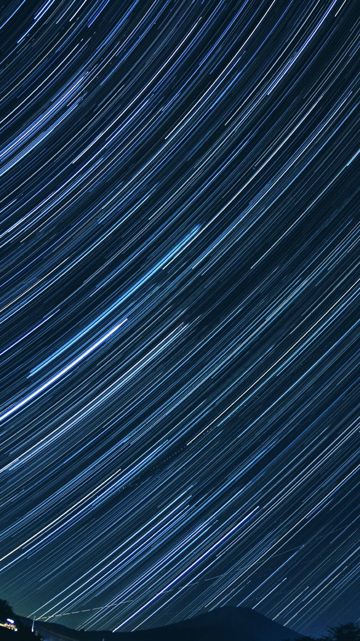 星軌太空手機壁紙 壁紙 — 星空條紋以鮮豔的藍色軌跡劃過夜間黑暗的山脈輪廓。