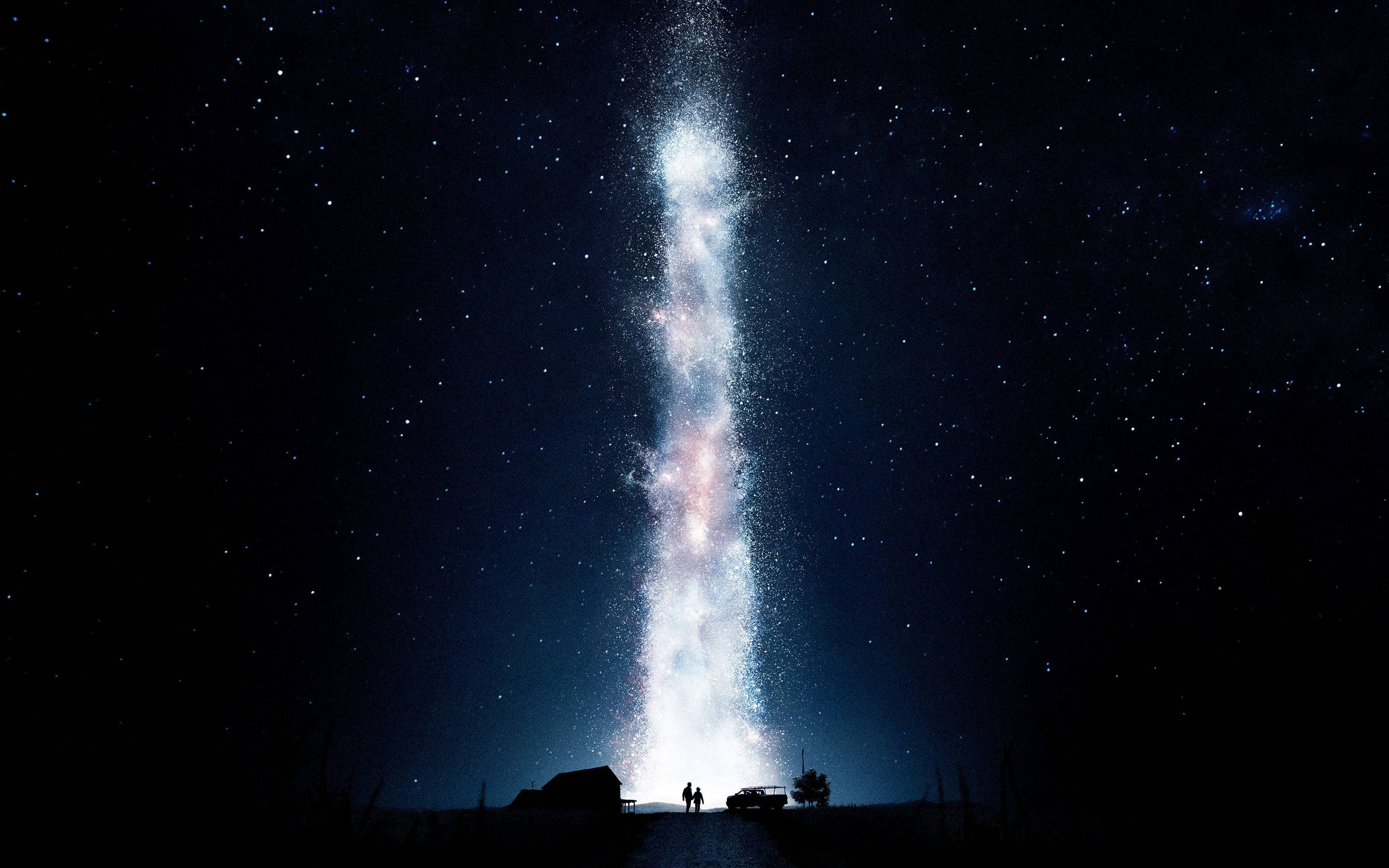 《星际穿越》地球夜間爆炸 壁紙 — 兩個剪影人物站在高聳、發光的銀河系下方，銀河系垂直延伸在繁星點點的夜空。
