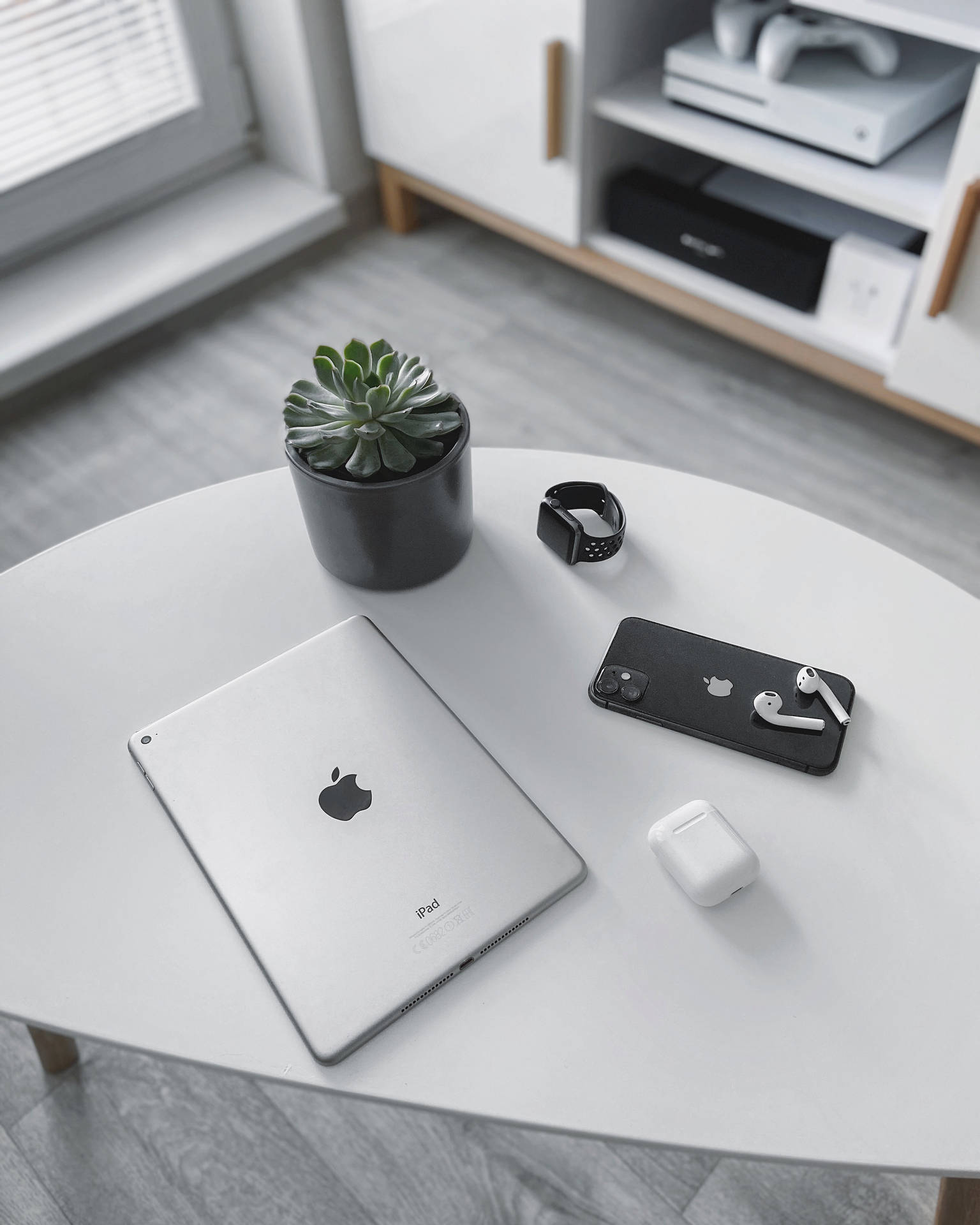 白色桌子上有iPad、電話、智能手錶、耳機和多肉植物，在現代房間中。