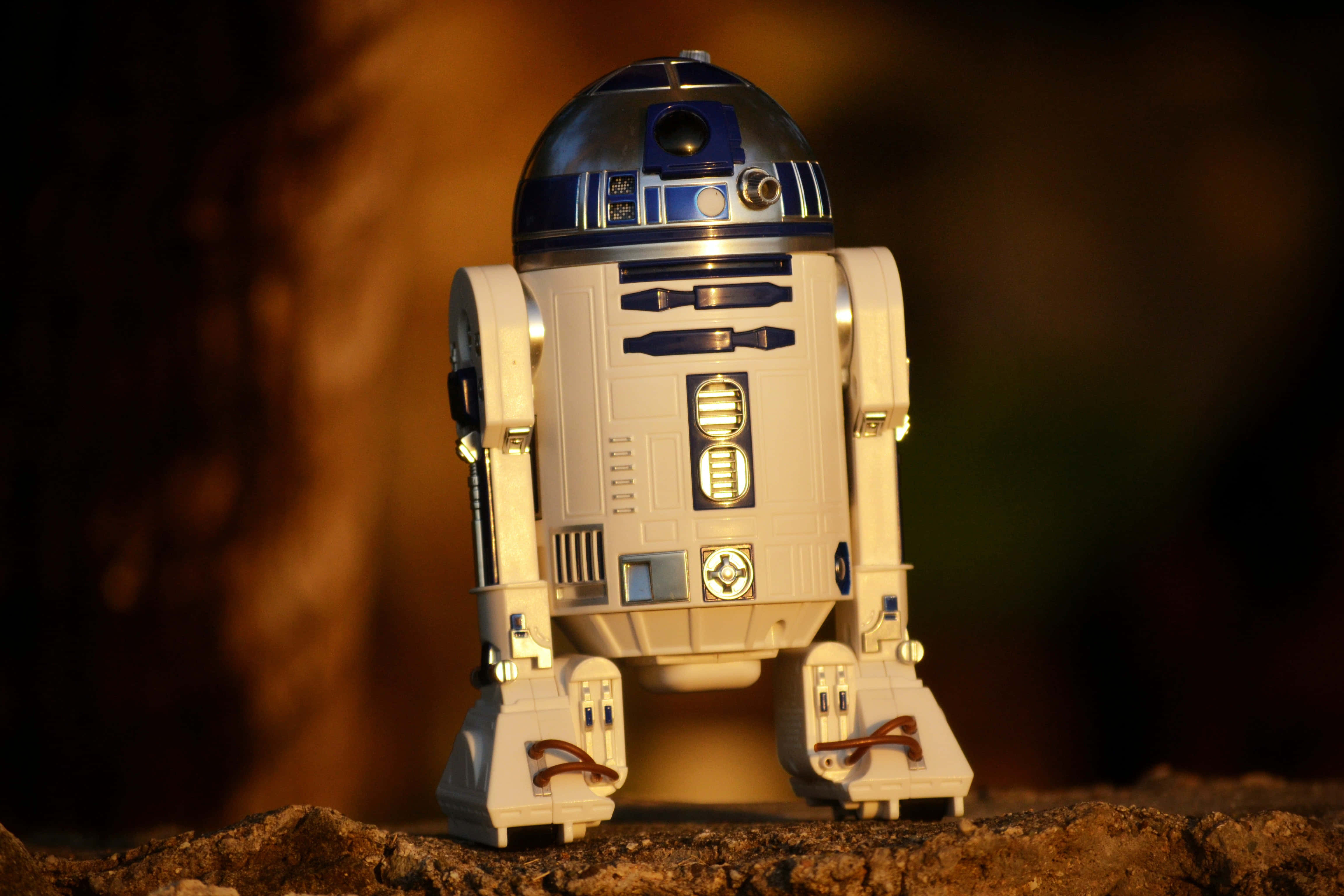 星際大戰經典角色R2-D2 壁紙 — 一個詳細的R2-D2機械人玩具站在岩石地形上，溫暖的金色燈光，背景模糊。