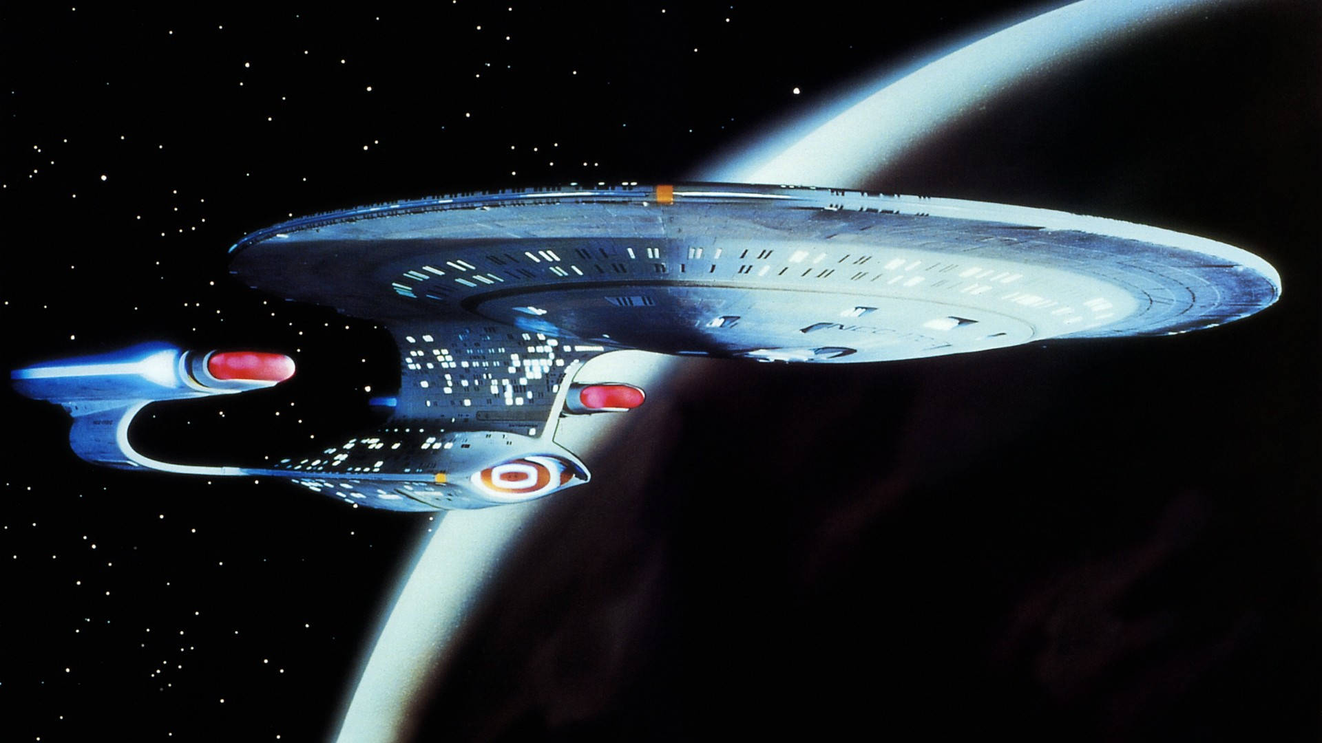 星際艦隊企業號高質桌面壁紙 壁紙 — 一艘星艦在星光璀璨的宇宙背景下，掠過一顆帶有發光環的行星。