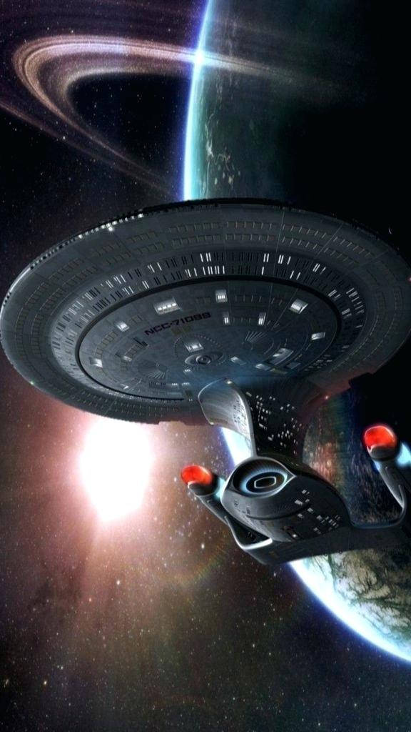 星際迷航：暗黑無垠 蘇聯企業號星艦 壁紙 — 一艘星際聯邦星艦在深空中滑過一顆帶環行星，背後有發光的星爆。