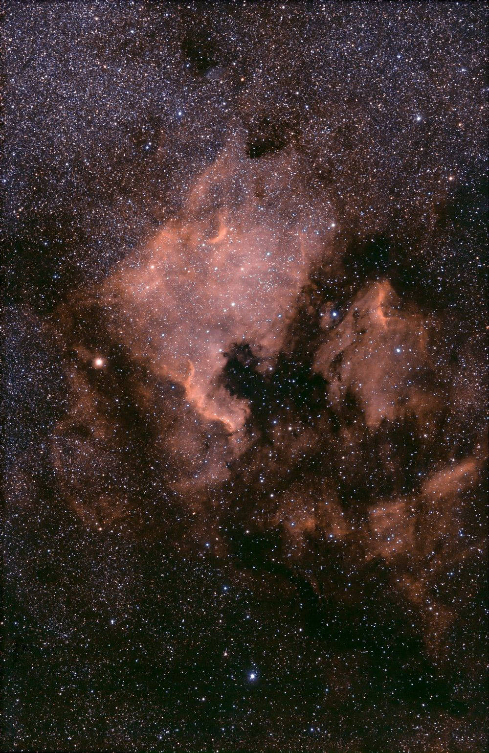 星雲宇宙棕色 iPhone 壁紙 — 一個宇宙星雲在深空星場背景下散發出火橙色和深紫色的光芒。