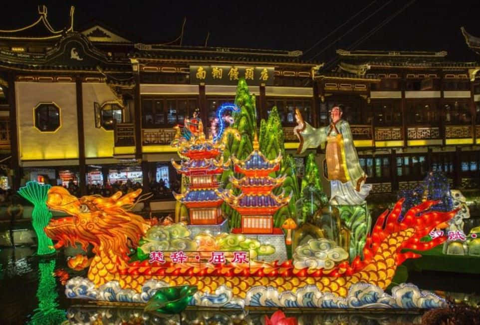 春節慶祝盛況空前 壁紙 — 一盞色彩鮮豔的發光龍燈籠在夜間漂浮在水面上，周圍是傳統的中國建築和閃爍的節日裝飾。