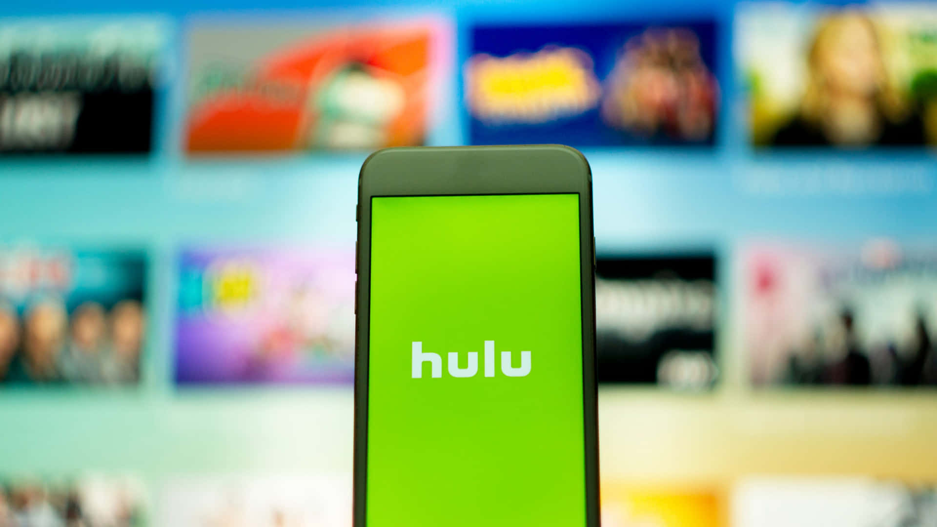 智能手機顯示 Hulu 應用程式標誌，背景為模糊的電視屏幕。