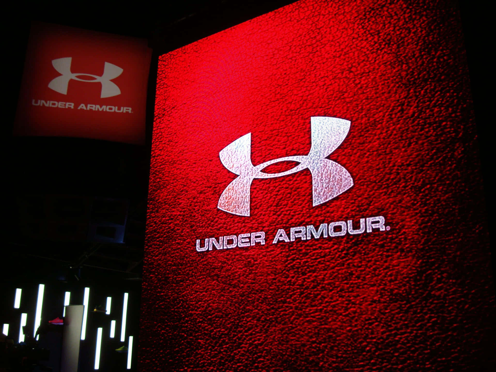 在黑暗房間的紅色紋理牆壁上照亮的 Under Armour 標誌。
