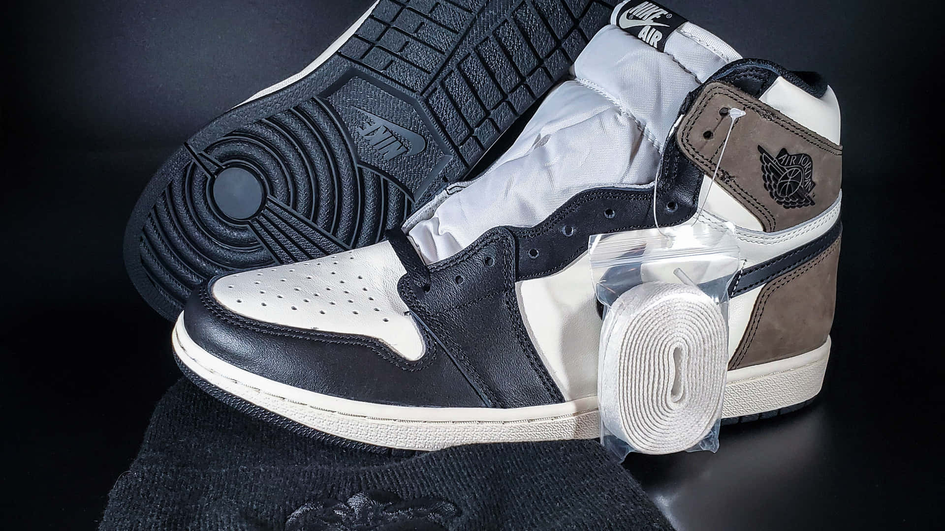 黑白 Air Jordan 1 運動鞋，帶有棕色點綴，未包裝並展示在深色表面上。