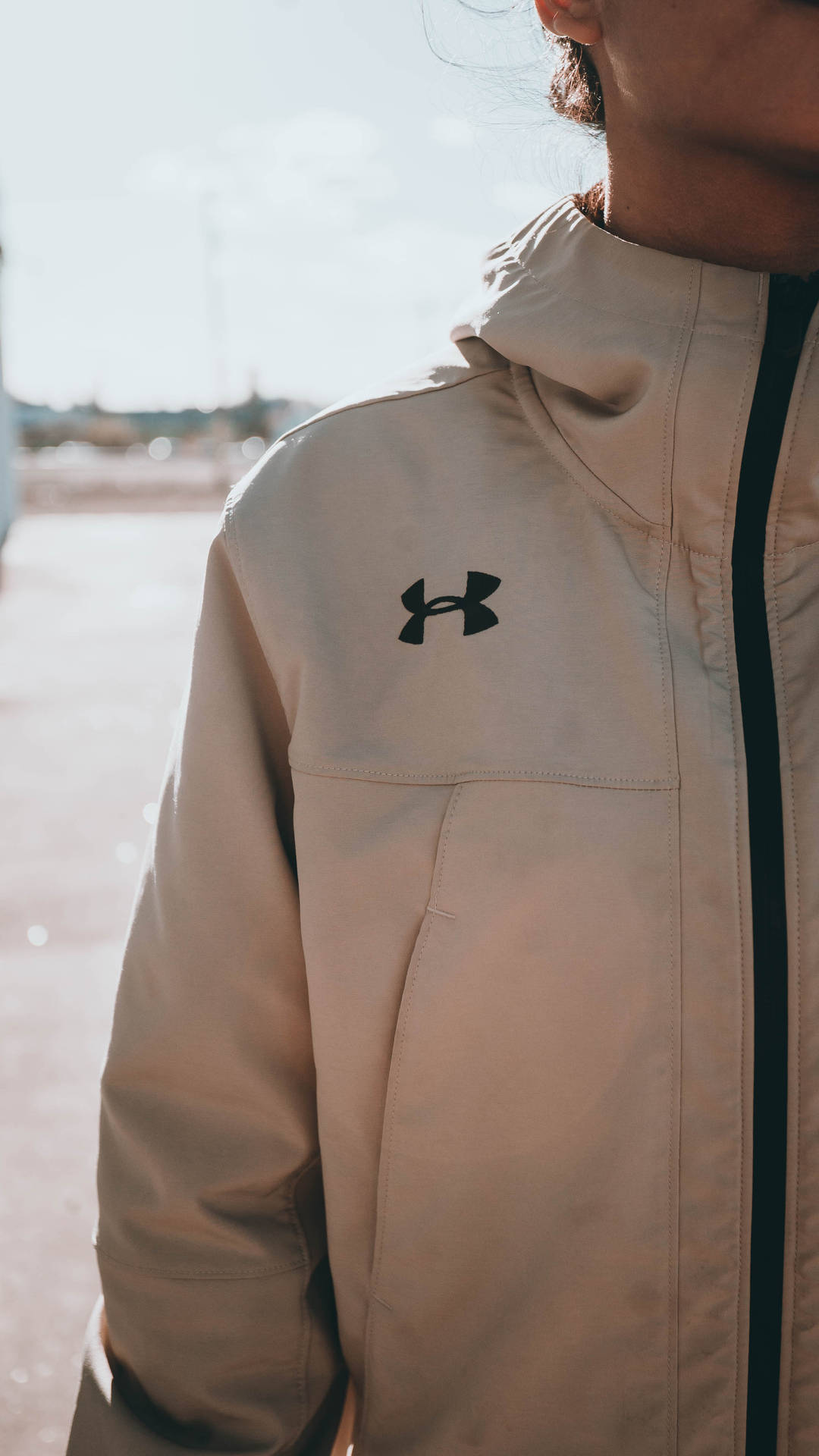一個人穿著米色 Under Armour 外套，配有黑色拉鍊和標誌。