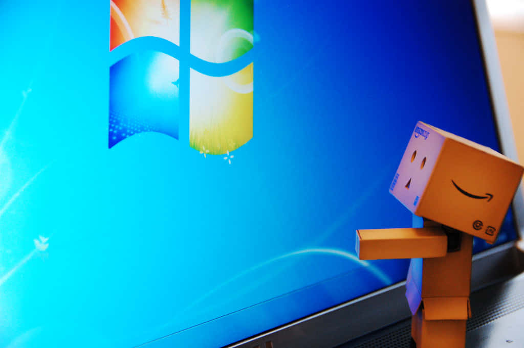 帶有亞馬遜標誌的紙板Danbo在顯示Windows 7桌面的筆記本電腦旁邊微笑。
