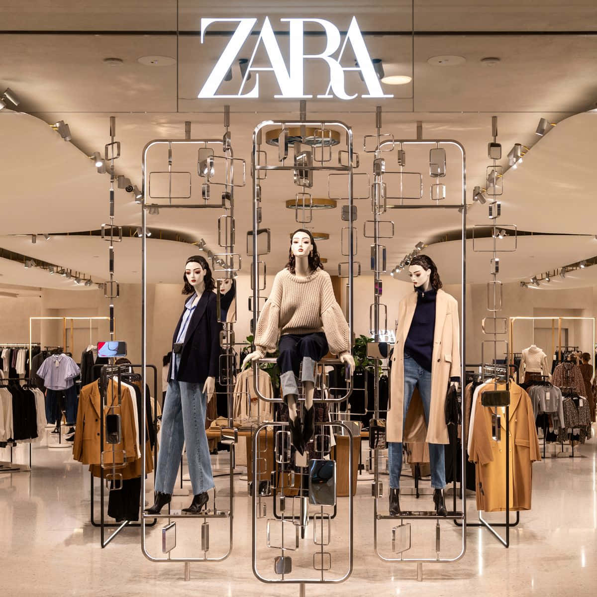 時尚、優雅的現代女性穿搭 壁紙 — Zara 店內的三個人體模型在幾何金屬框架和溫暖燈光下展示秋季時裝。