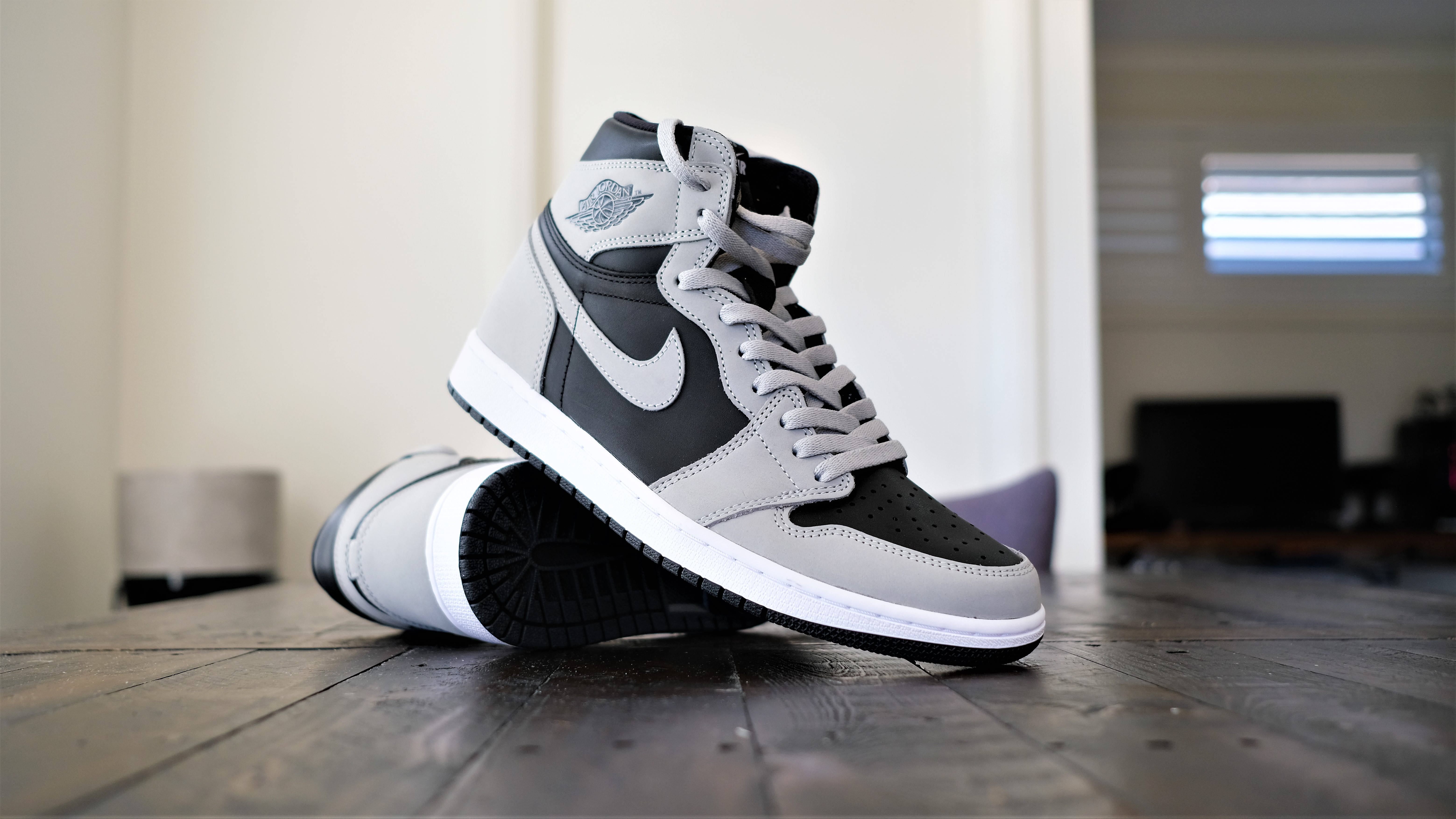 時尚Air Jordan銀色球鞋 壁紙 — 一雙時尚的灰黑色高筒運動鞋放在室內柔和光線下的深色木地板上。