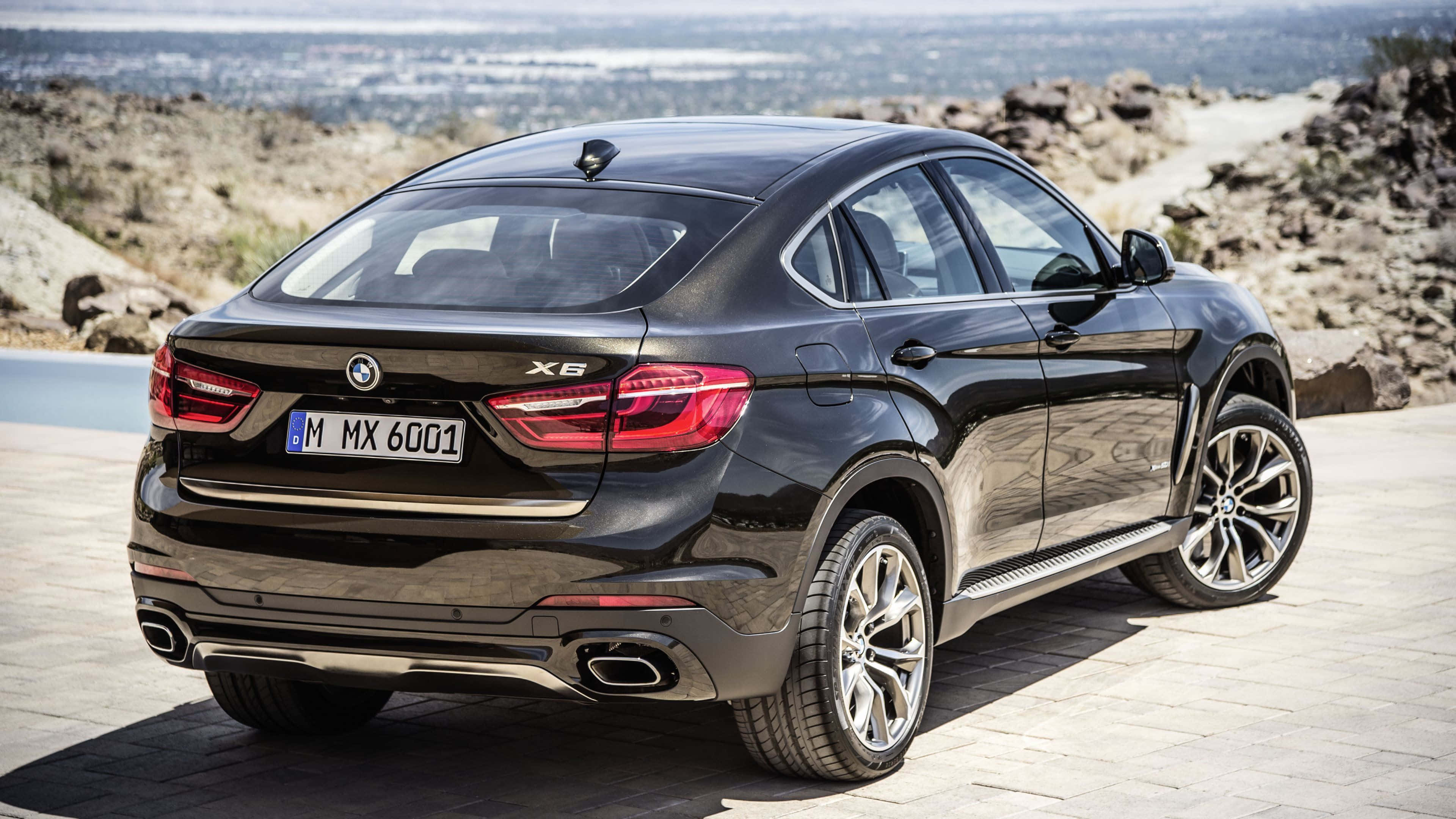 時尚BMW X6盡顯風采 壁紙 — 一輛時尚的黑色BMW X6 SUV停泊在石頭觀景台上，遠方城市景觀在明亮日光下清晰可見。