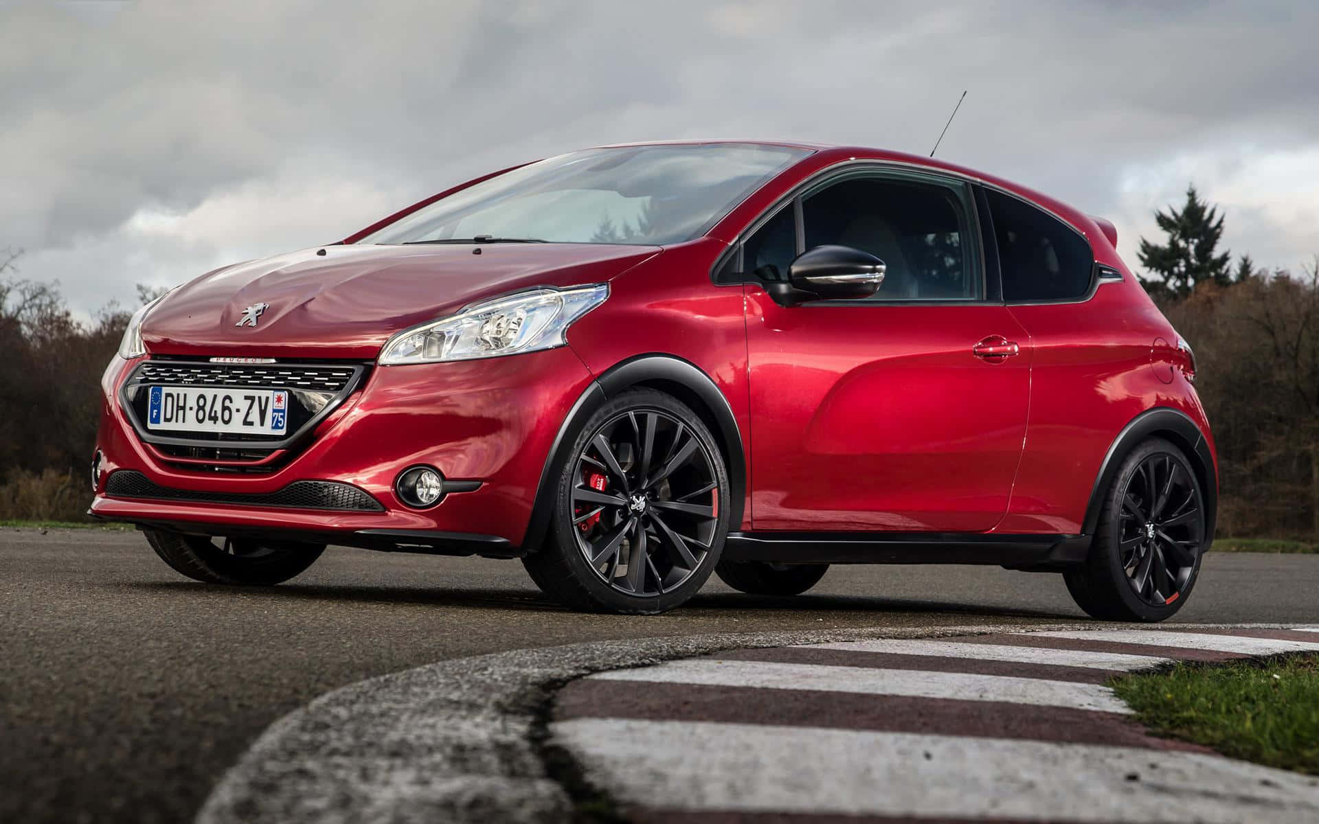 時尚Peugeot 208停泊城市街頭 壁紙 — 一輛亮紅色Peugeot 208 GT Line跑車停泊在賽道邊緣，背景是陰天和樹木。