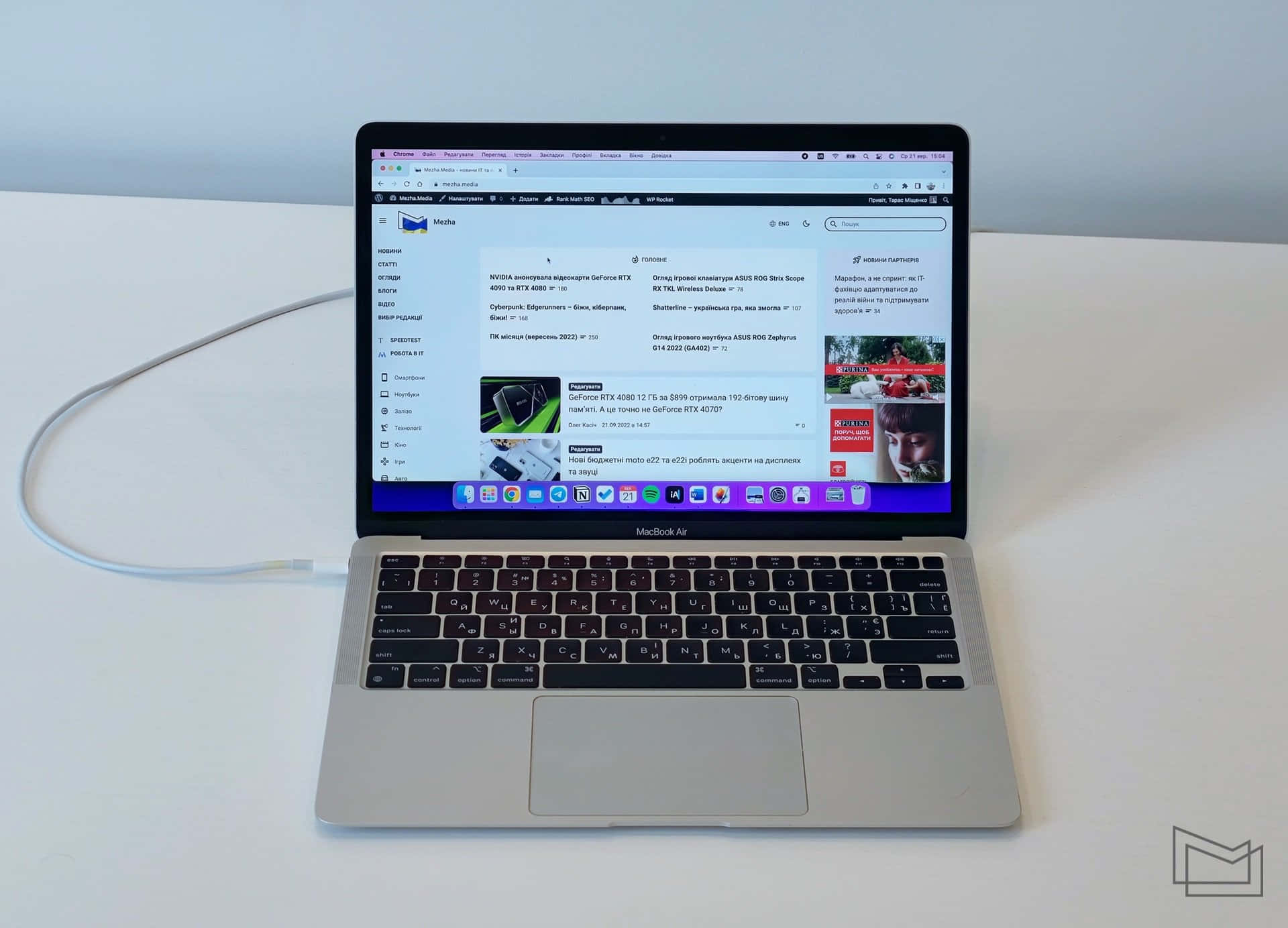 時尚優雅的 Apple MacBook 壁紙 — 一部銀色 MacBook Air 手提電腦打開放在白色桌子上，顯示一個俄羅斯科技新聞網站，並插著一條電線。