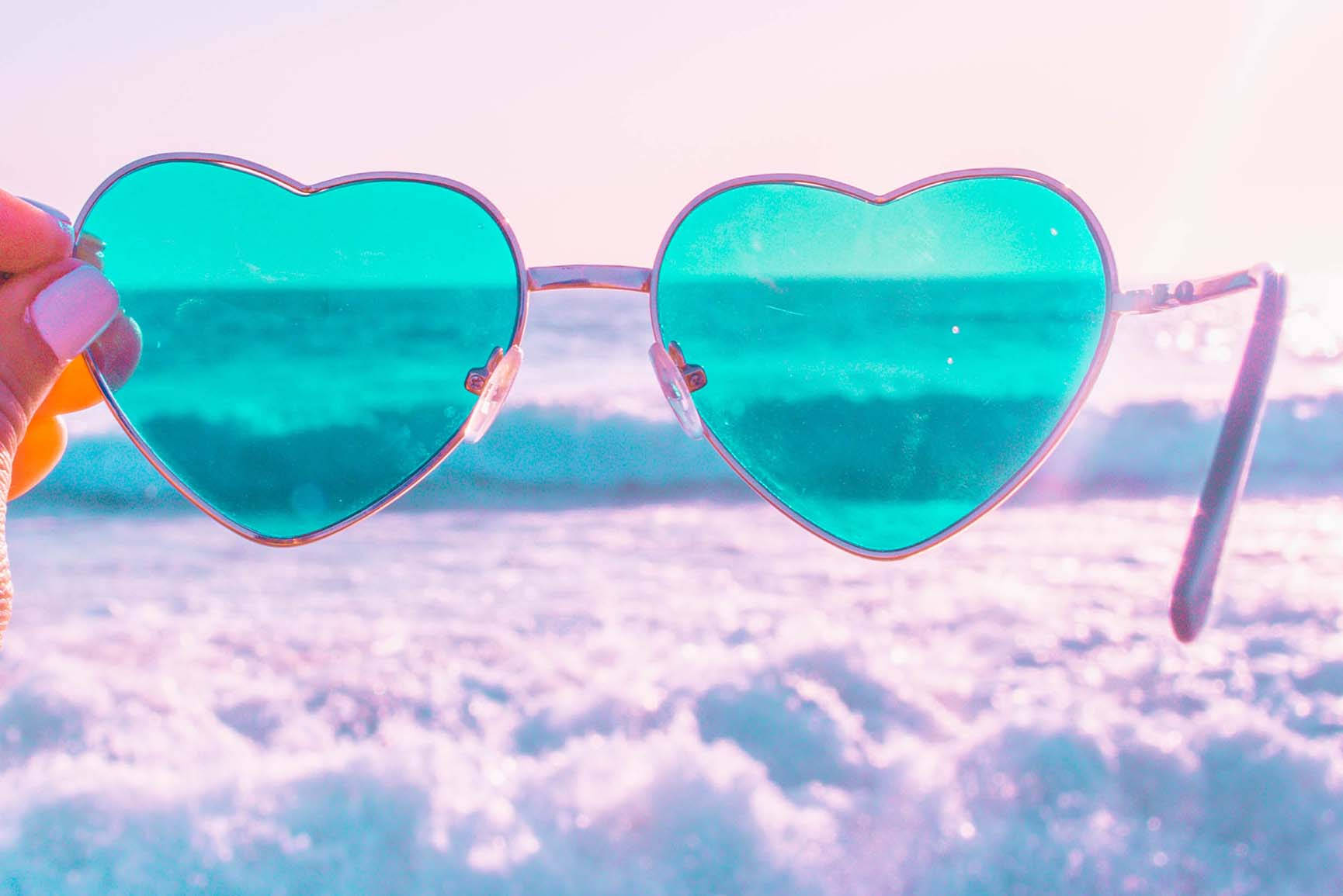 手裡拿著心形太陽眼鏡，在粉彩海灘上反射著海浪。 — 夏季 壁紙