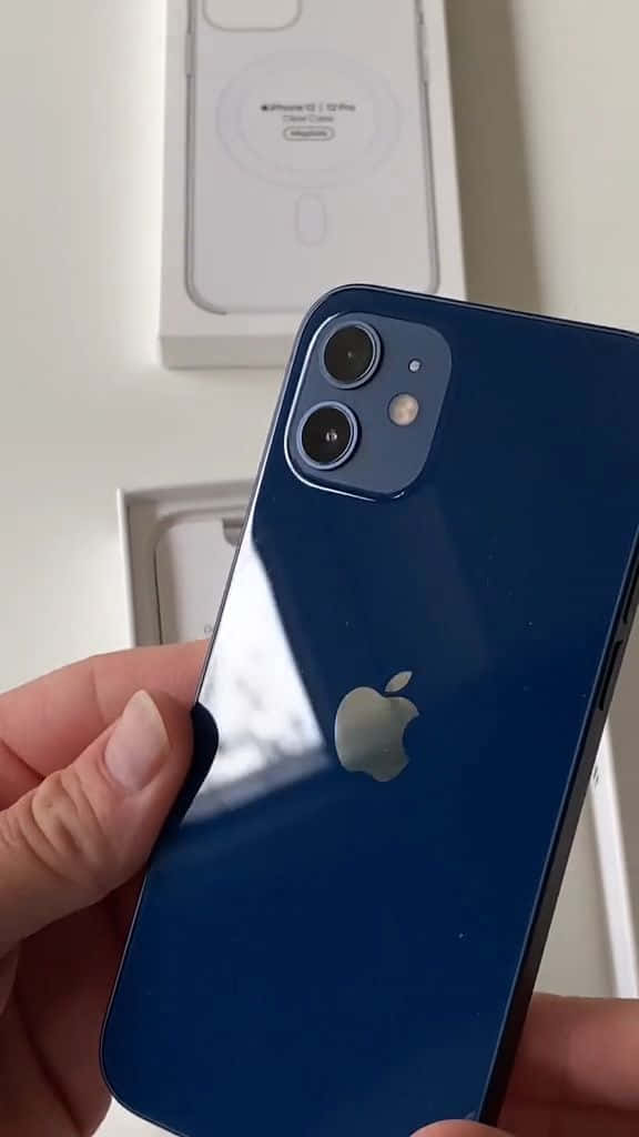 時尚多彩的 Apple iPhone 12 壁紙 — 一隻手拿著藍色iPhone 12 mini，相機模組在白色盒子背景上可見。