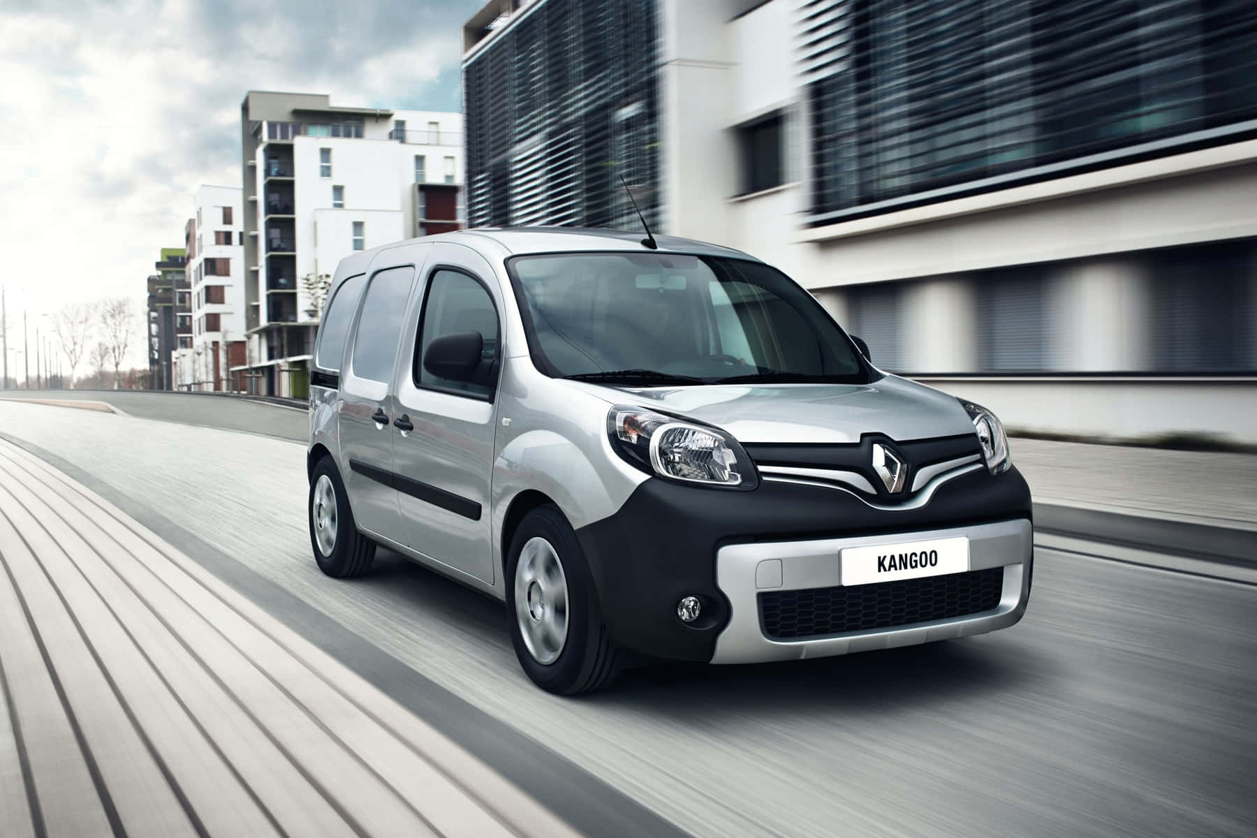 時尚多用途Renault Kangoo城市停泊 壁紙 — 一輛銀色雷諾Kangoo客貨車在現代城市街道上飛馳，人行道和建築物呈現動態模糊效果。