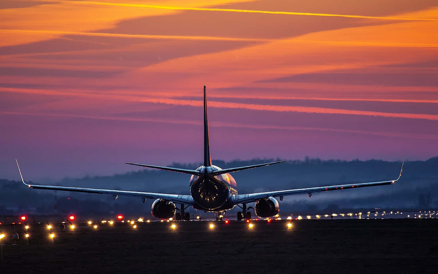 時尚天空飛機背景風景 壁紙 — 一架商用飛機在黃昏時停在跑道上，上空有鮮豔的橙色和紫色天空條紋。