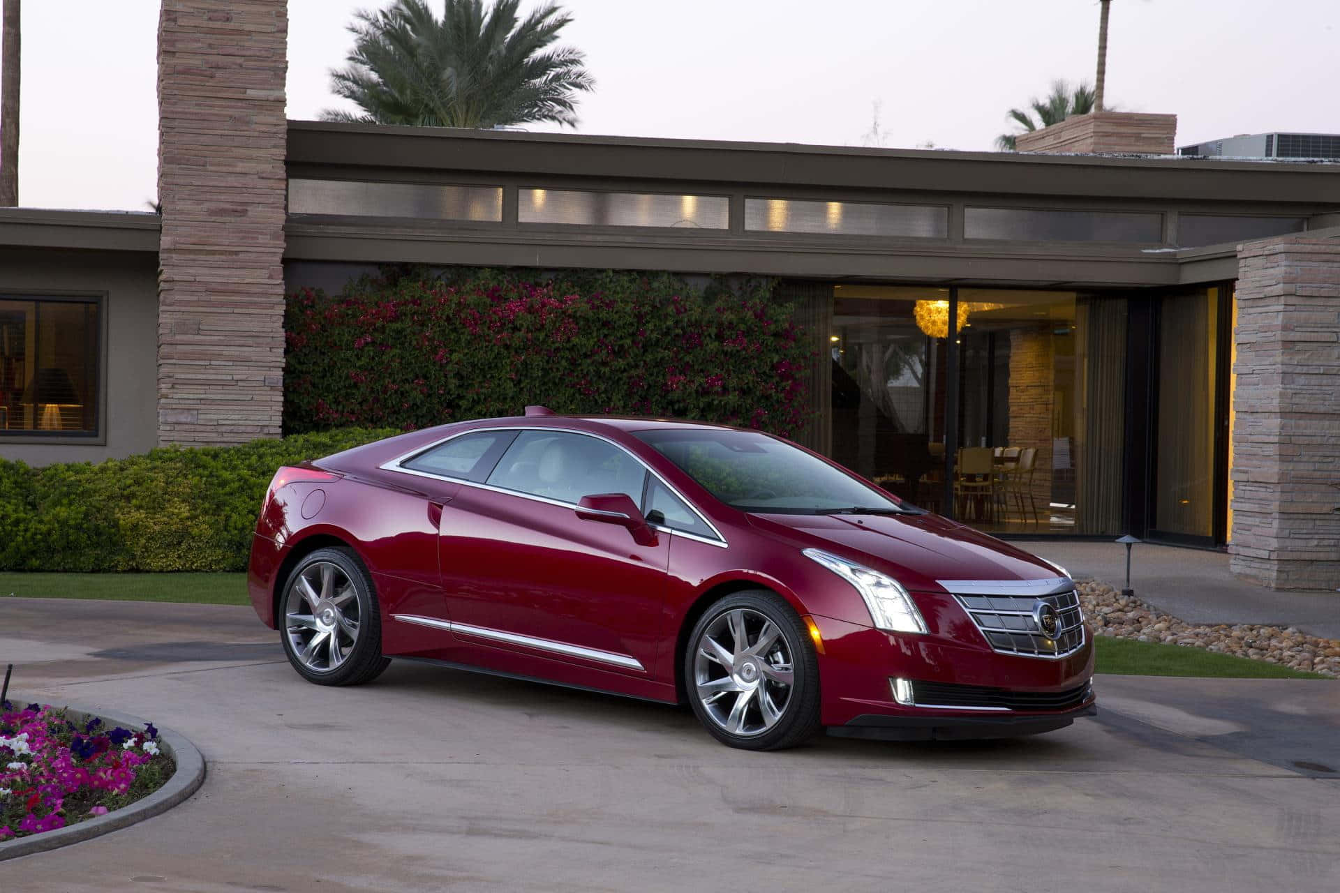 時尚奢華的電動車——凱迪拉克ELR 壁紙 — 一輛光亮的紅色Cadillac ELR雙門轎跑車停泊在現代化住宅前的鋪砌車道上，住宅周圍有棕櫚樹和開花的灌木叢。