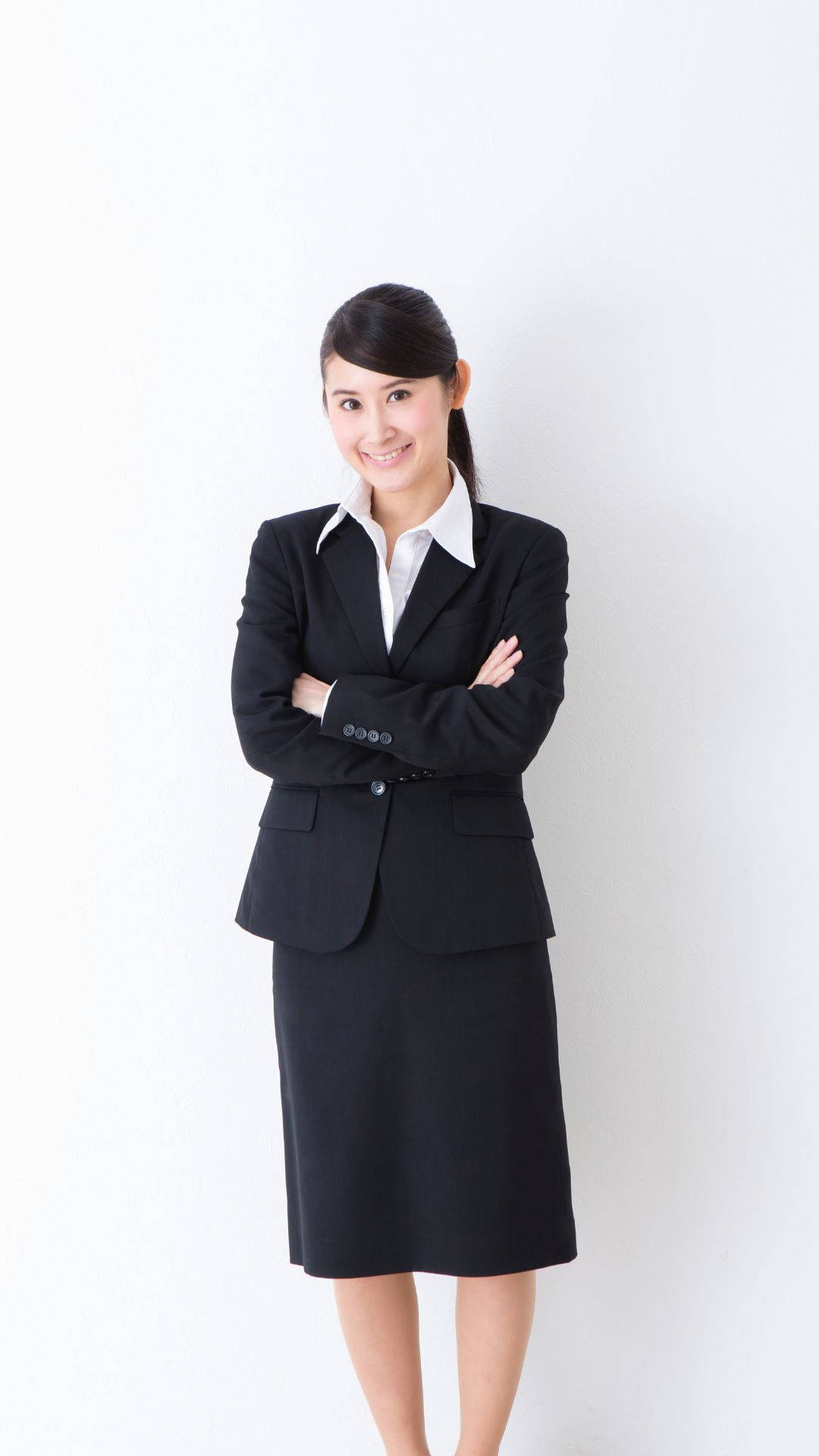 時尚女性穿黑色西裝裙 壁紙 — 一位自信的商務女性穿著黑色西裝，在純白背景前交叉雙臂微笑。