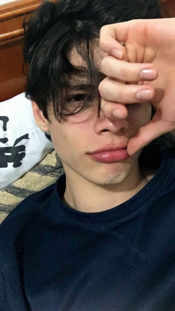 時尚少年在公園拍攝完美照片 壁紙 — 一位深色頭髮的年輕人躺在圖案沙發上，將手放在一隻眼睛上，穿著深藍色襯衫。