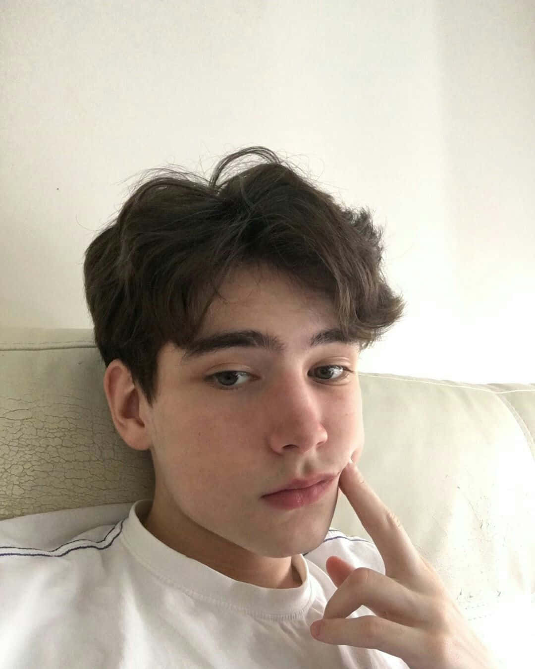 穿白恤衫的年輕男子在梳化上休息，手指放在臉頰上 — 美學男孩 壁紙
