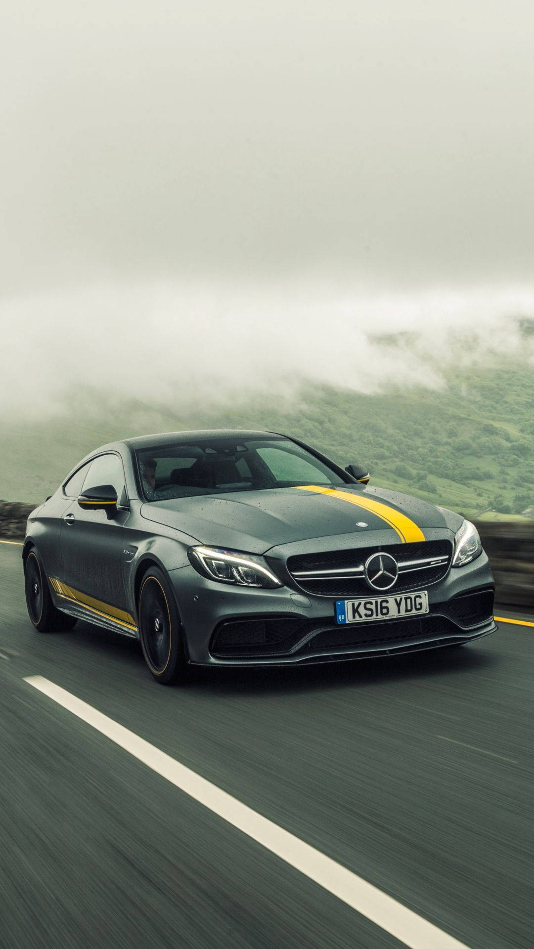 灰色 Mercedes-AMG C63 S Coupe 帶有黃色條紋在霧氣瀰漫的山路上行駛。