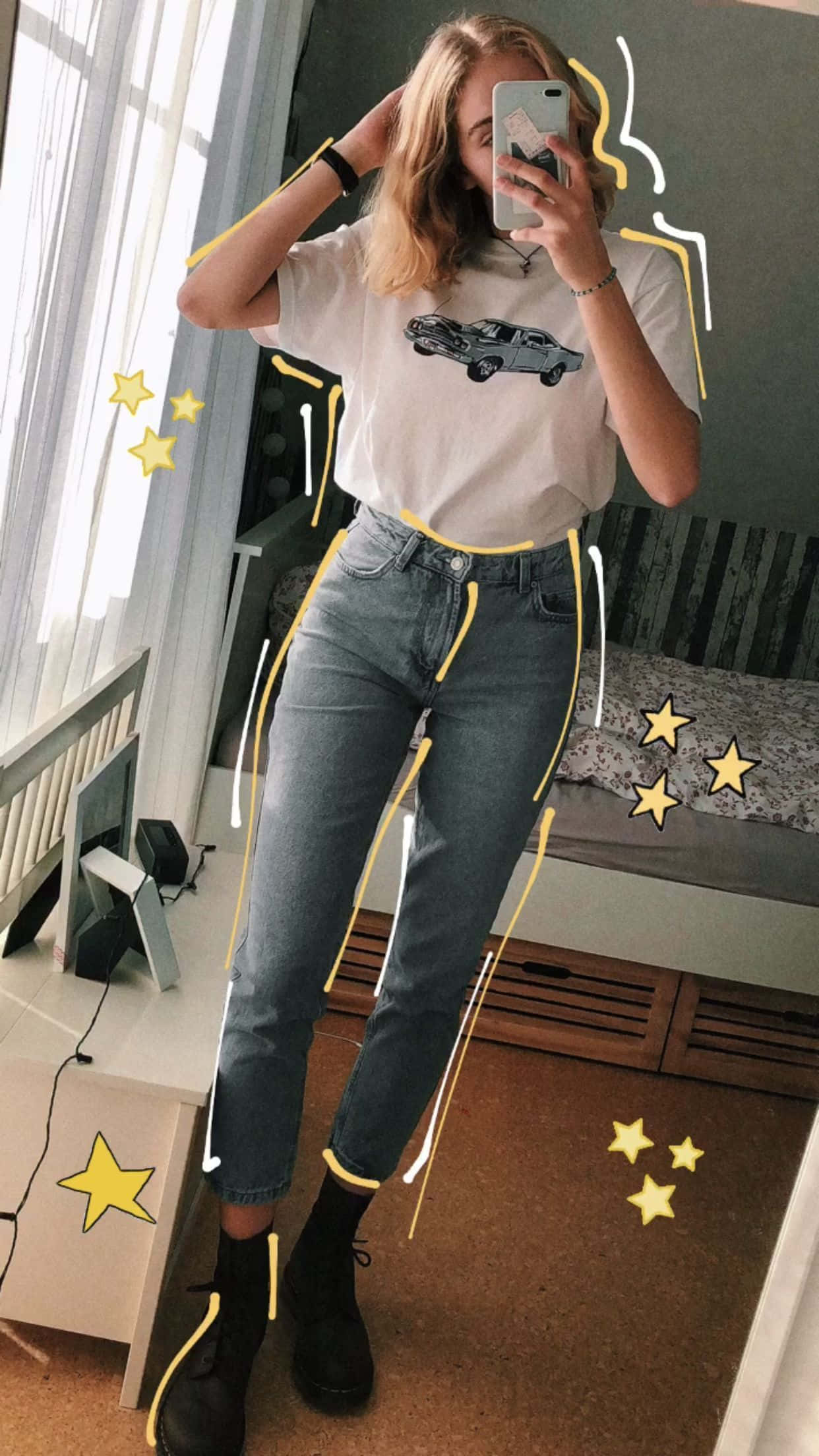 時尚潮流服裝的豐富選擇 壁紙 — 一位年輕女性在臥室裡對著鏡子自拍，穿著汽車圖案T恤和帶有黃色塗鴉點綴和星星貼紙的牛仔褲。