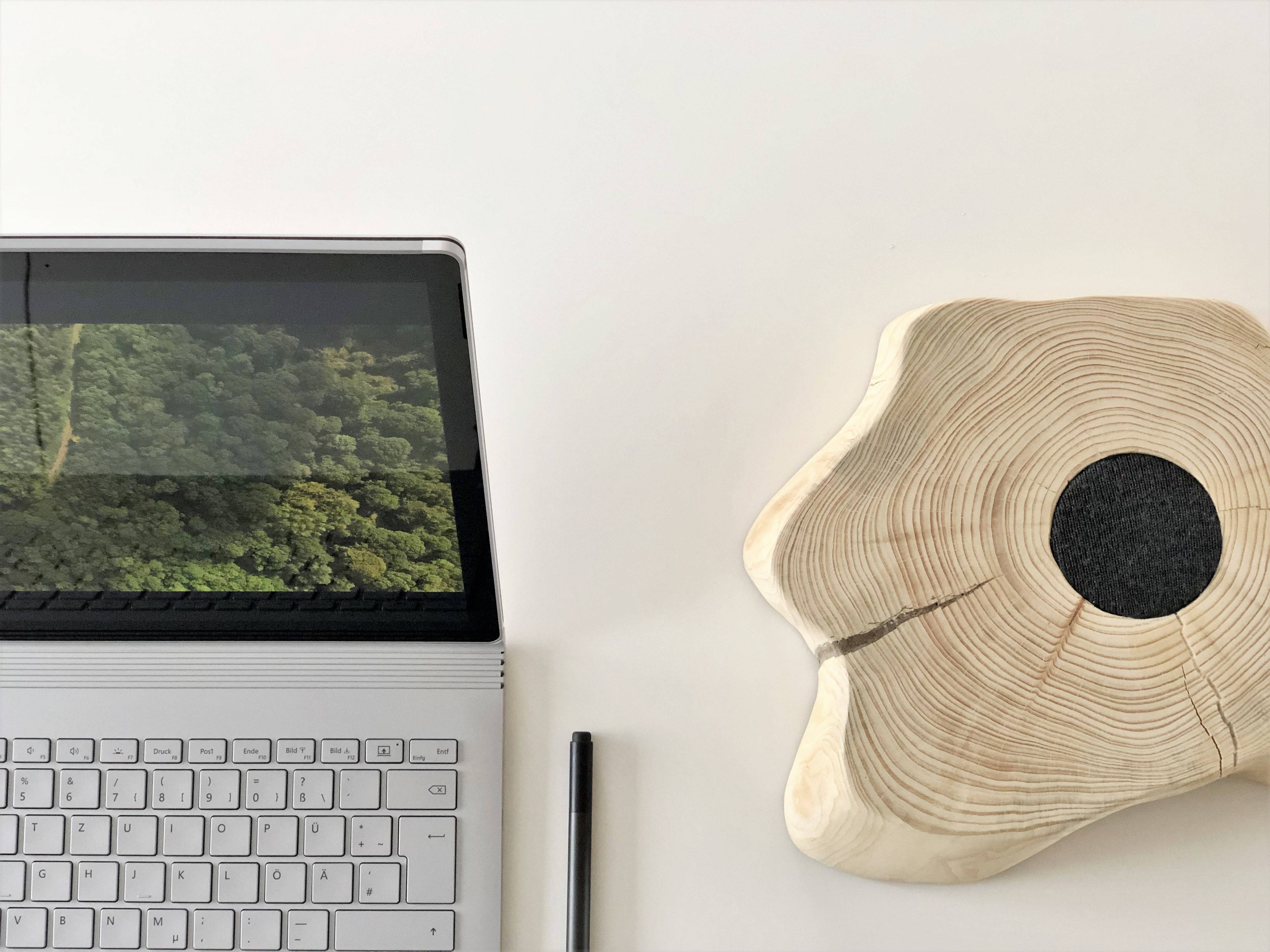 時尚現代的 Surface Book 3 壁紙 — 極簡白色桌面設置，配備銀色手提電腦，顯示茂密綠色森林和獨特的黑色中心木片。