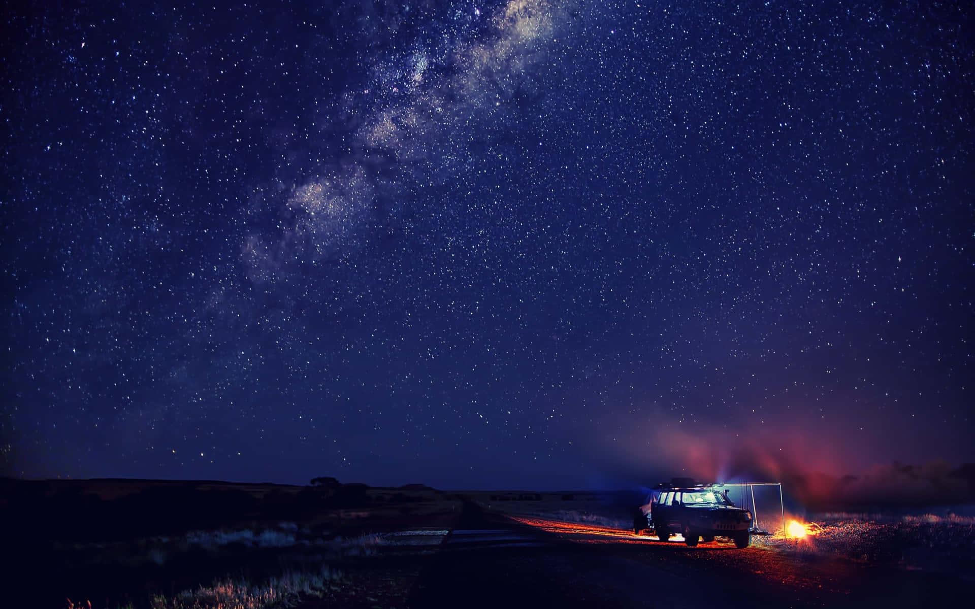 一輛汽車在夜晚停在沙漠公路上，星空下，附近有營火。