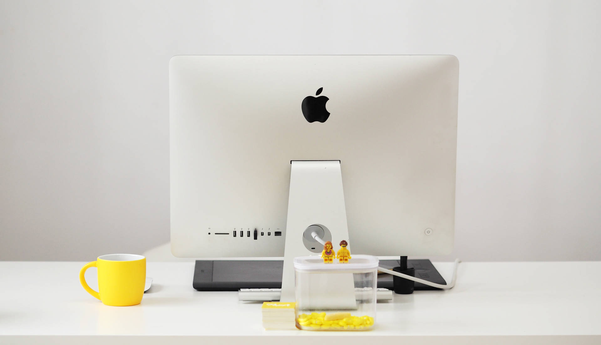 乾淨的白色桌面，配有 Apple iMac、黃色馬克杯和 LEGO 人仔。