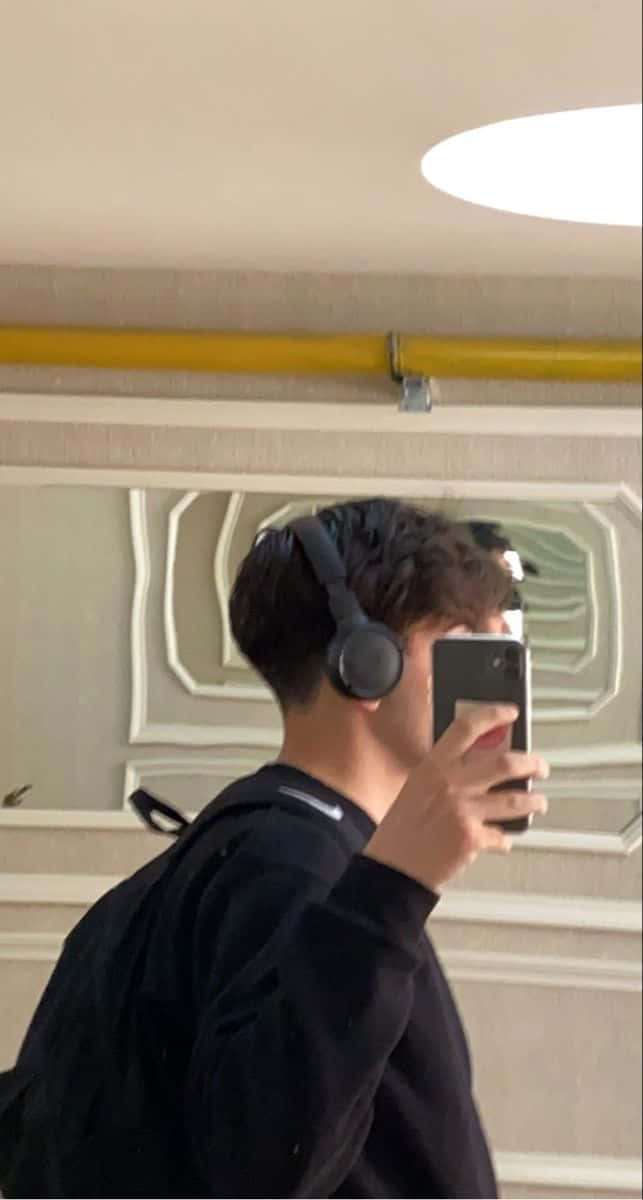 年輕男子在室內戴著耳機對著鏡子自拍