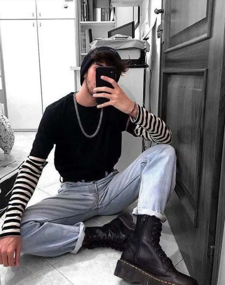 時尚男孩沐浴在陽光的寧靜中 壁紙 — 一個戴冷帽、穿條紋袖嘅年輕男子坐喺瓷磚地板上面，用手機影緊鏡中自拍。