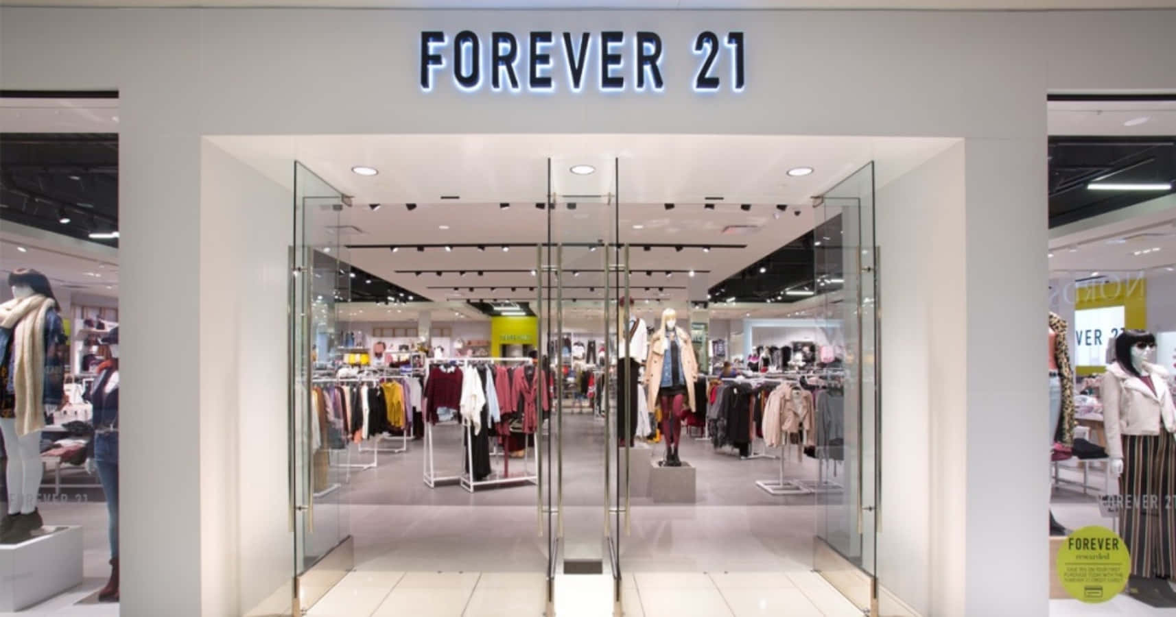 時尚百搭，Forever 21 為你打造每場場合的完美造型 壁紙 — 燈光明亮的Forever 21商店入口，玻璃門內展示著色彩繽紛的衣物架和模特兒。