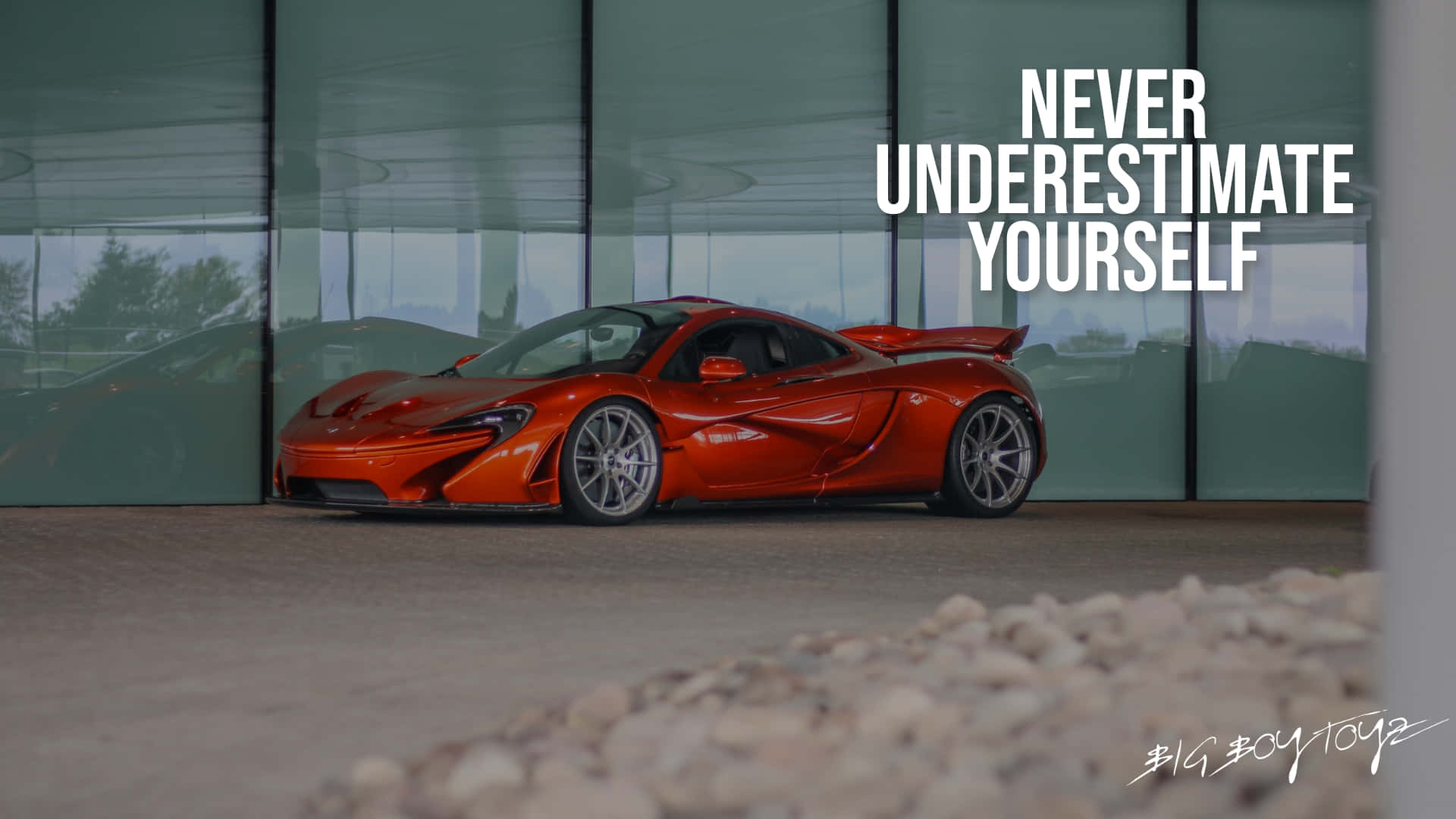 橙色McLaren P1超級跑車在玻璃建築內，帶有勵志文字。