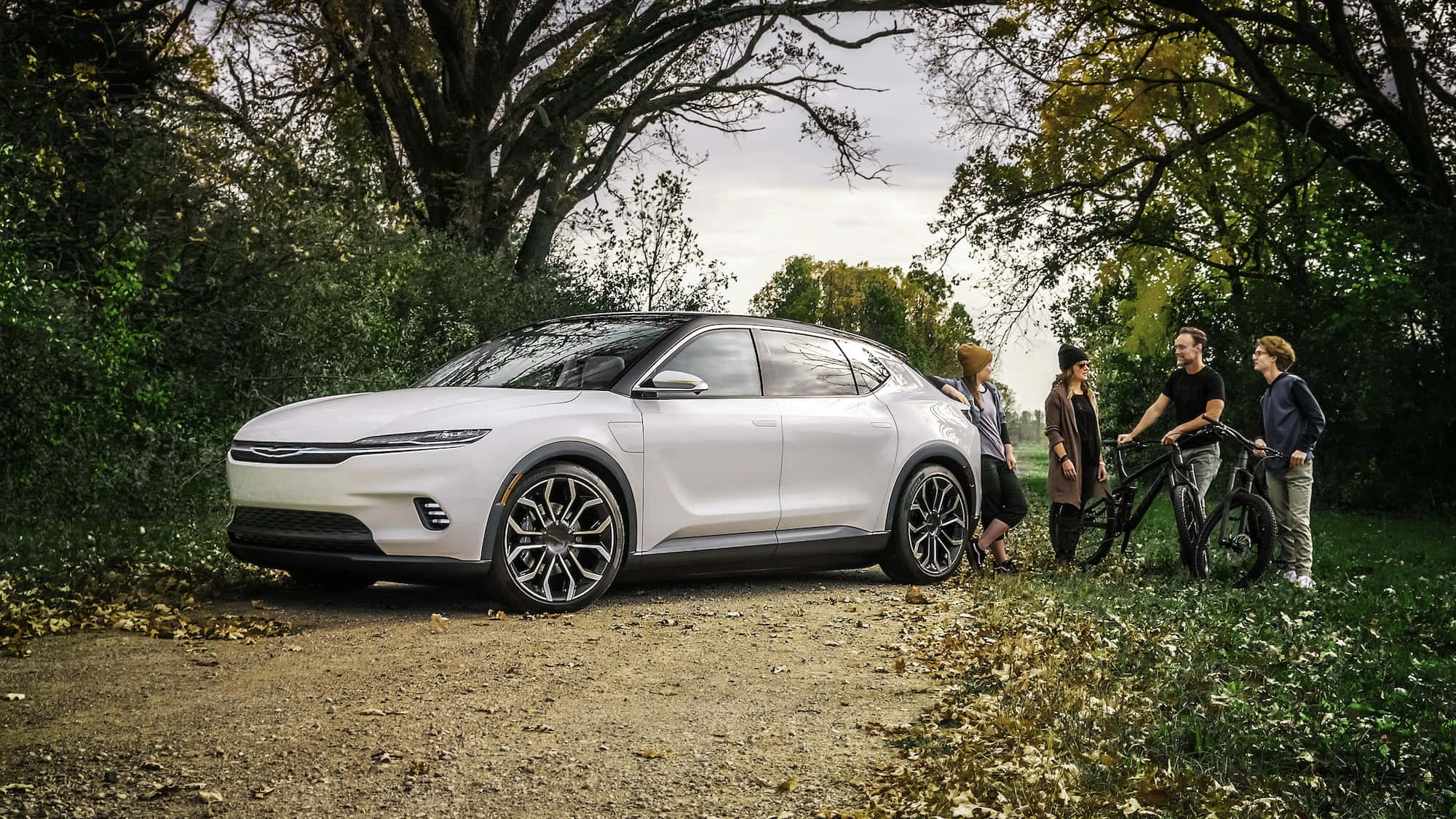 時尚精緻的 Chrysler 300 壁紙 — 一架時尚的白色電動SUV停泊在鋪滿落葉的泥路上，一家大小踩著單車在秋樹下欣賞它。