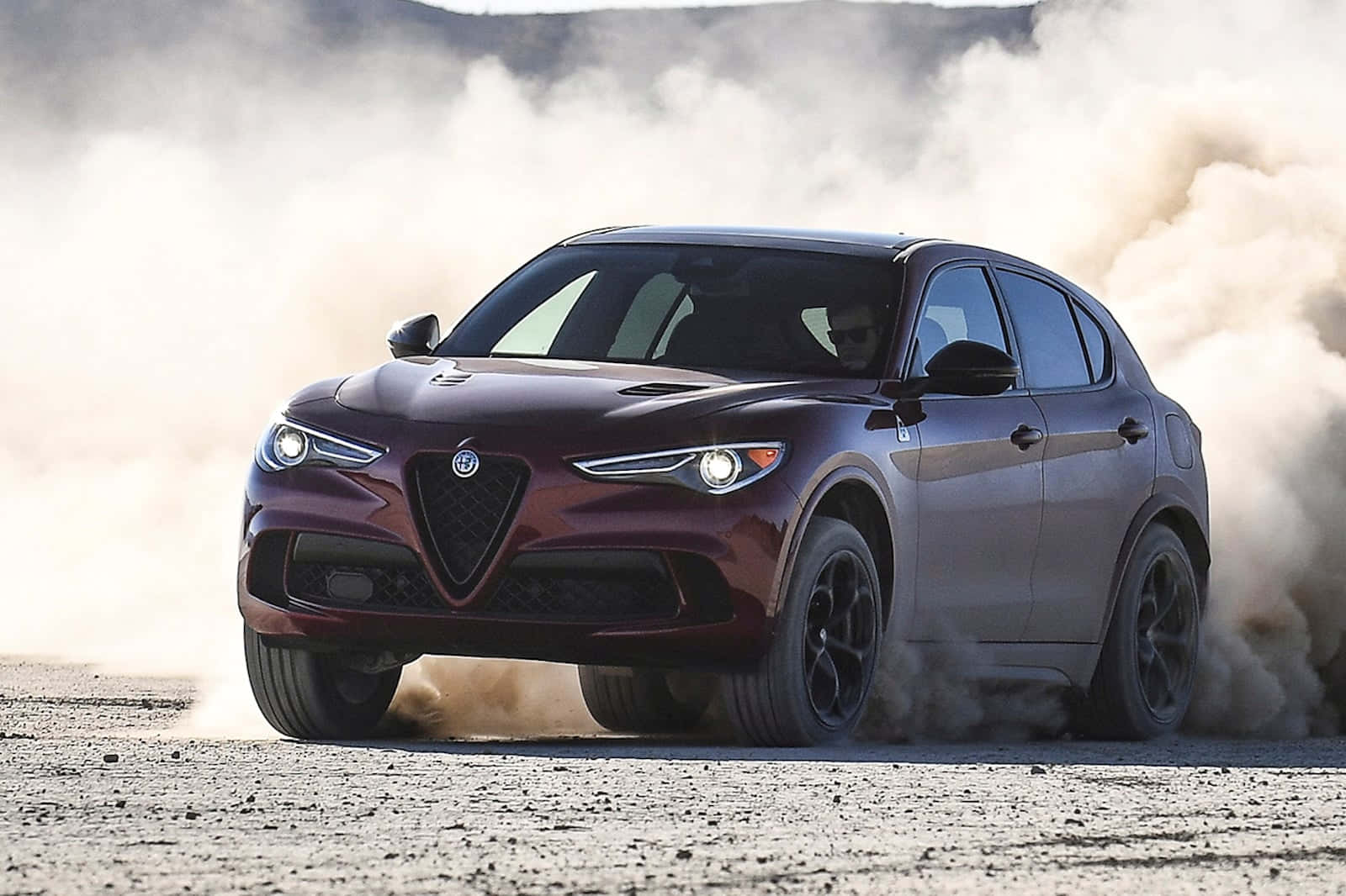 時尚經典的Alfa Romeo，展現永恆風格 壁紙 — 一輛栗色Alfa Romeo SUV在塵土飛揚的沙漠景觀中奔馳，揚起沙塵和礫石。