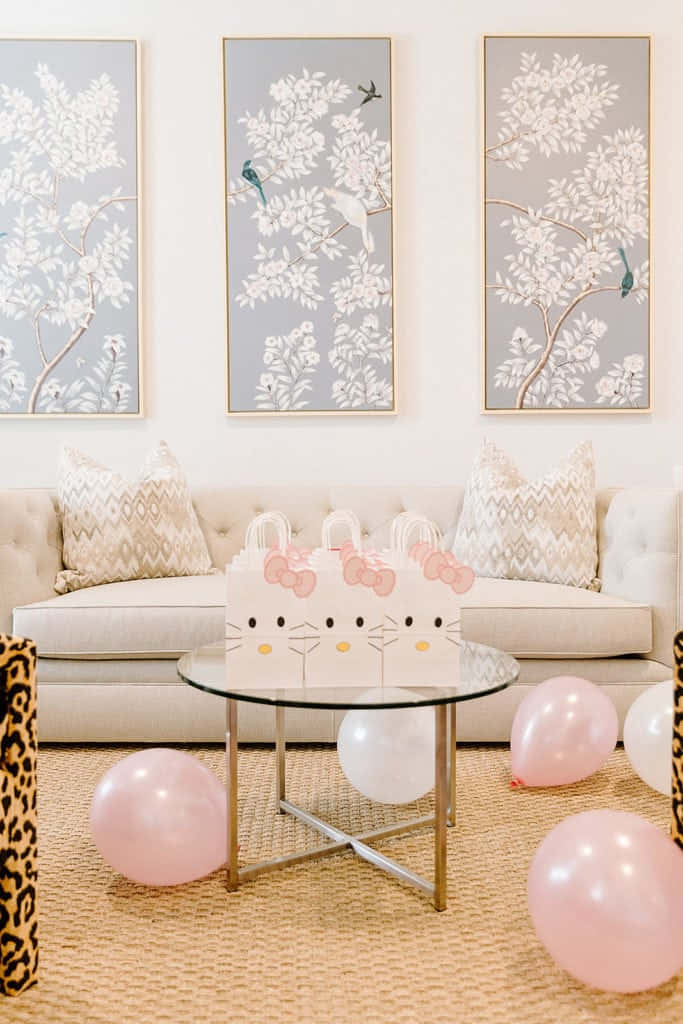 Hello Kitty Party 桌布 壁紙 — 時尚育嬰室，配有米色梳化、圖案抱枕，上方掛有三幅裱框植物畫，周圍環繞著粉紅色和白色氣球以及Hello Kitty禮物袋。